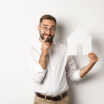 Imagen de un hombre pensando mientras busca apartamento sosteniendo modelo casa de papel