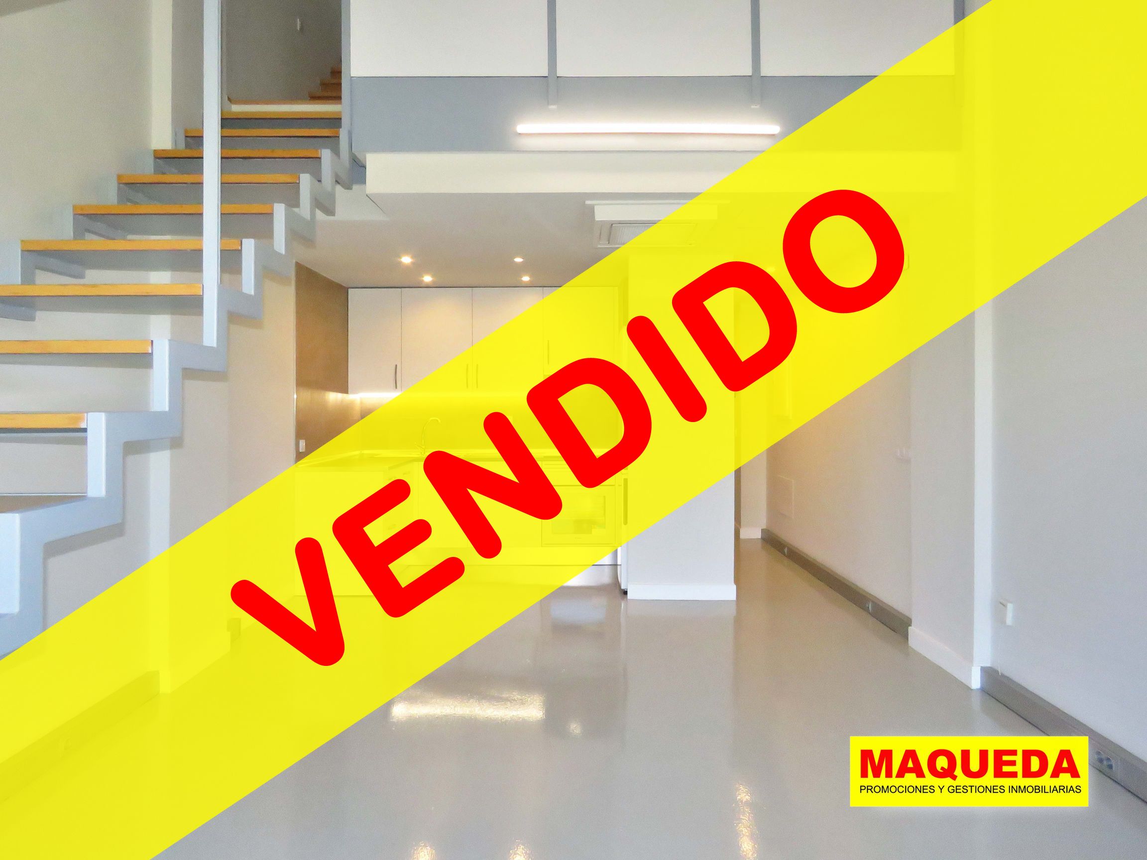 Sala diáfana con escaleras y cocina americana al fondo. En primer plano figura la etiqueta de VENDIDO