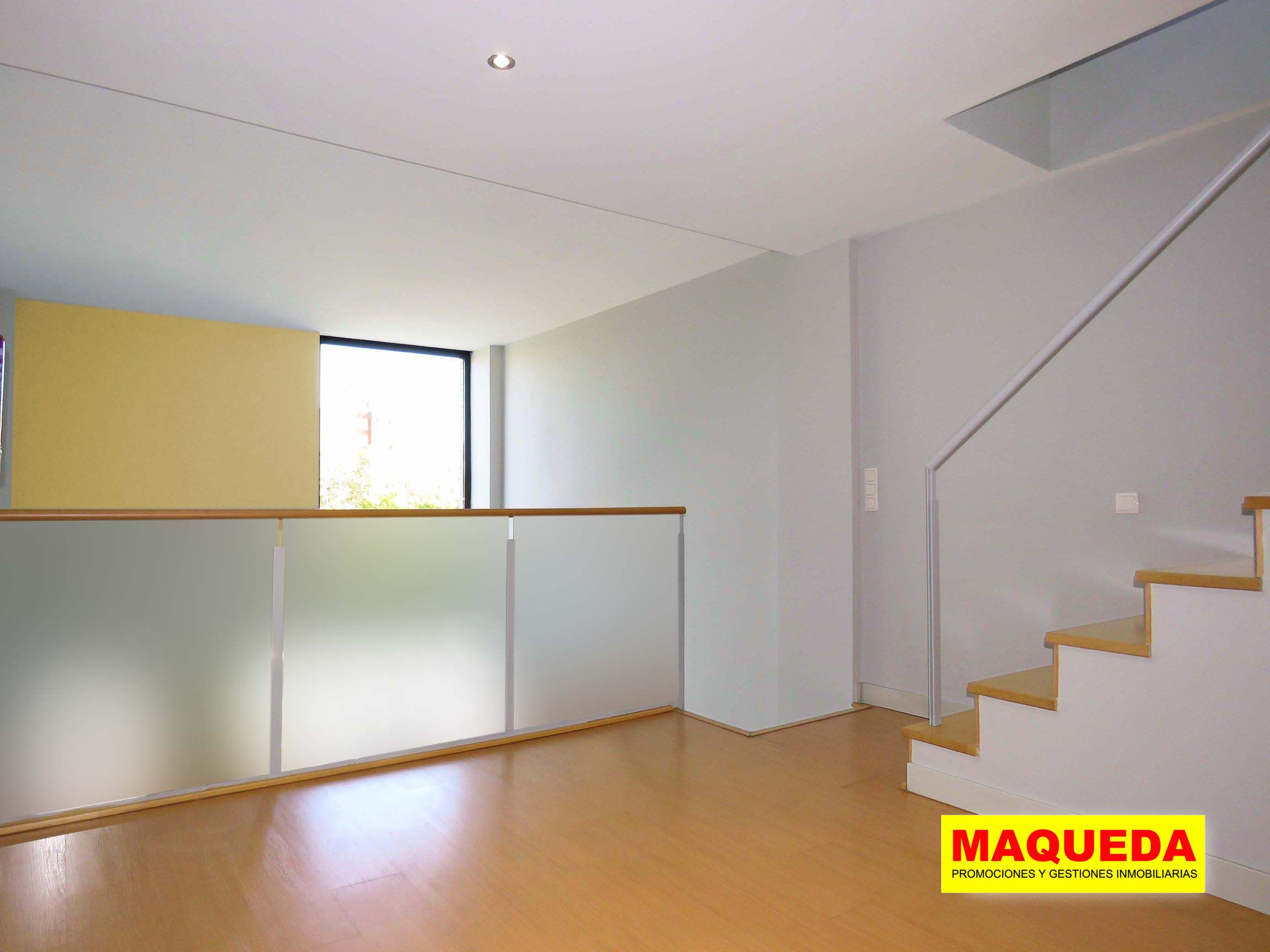 Habitación en planta alta con suelo de tarima y escalera a la azotea. Tras la barandilla, amplio ventanal.