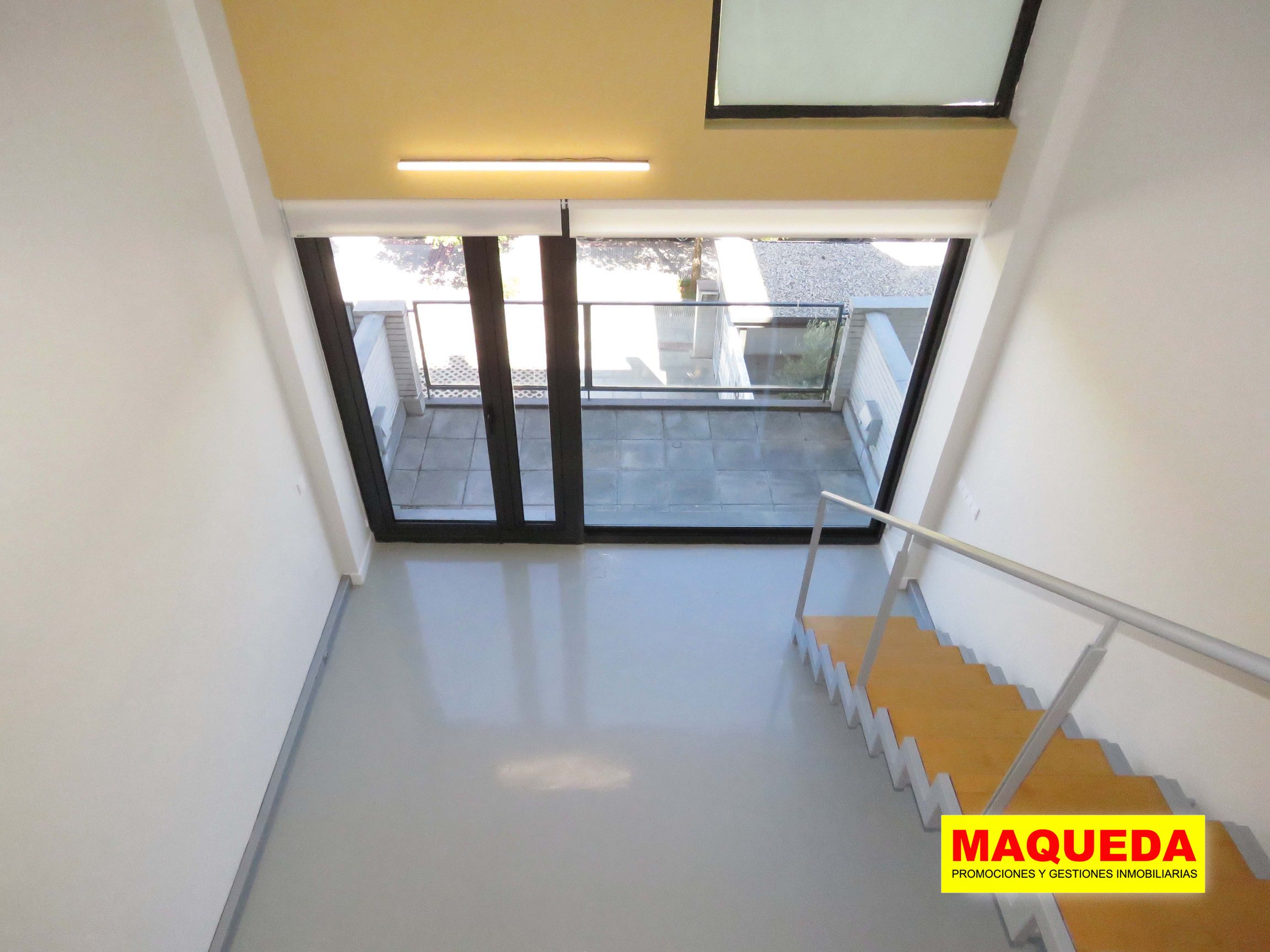 Vista inclinada de la sala en planta baja con ventanal y acceso a la terraza desde la habitación de la planta alta