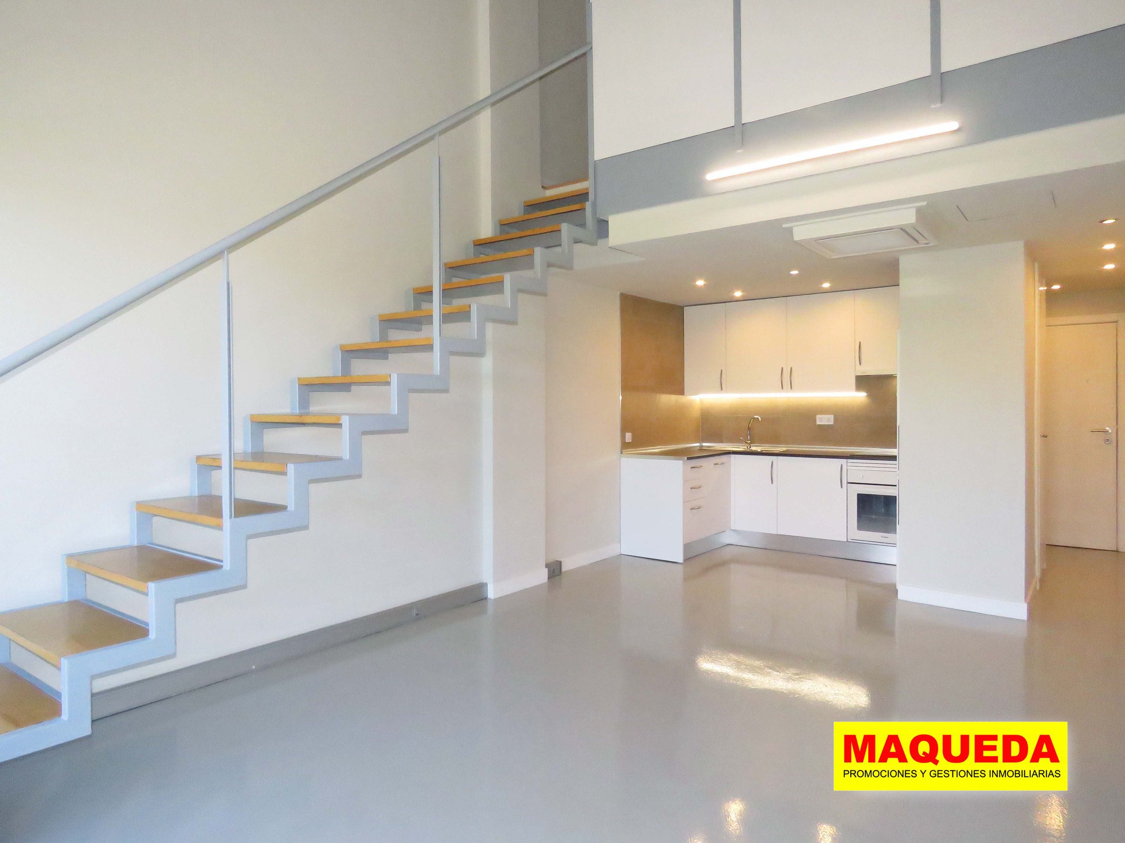 Sala diáfana con escaleras y cocina americana al fondo