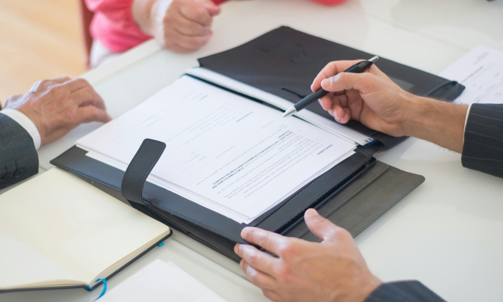 Primer plano de las manos de un asesor sobre unos documentos, explicando algo a una pareja