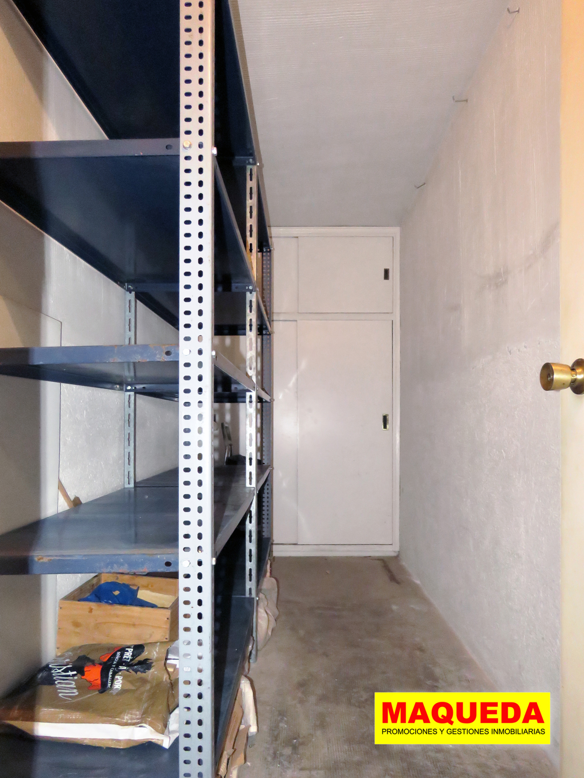 Trastero de la vivienda con estanterías metálicas y armario al fondo