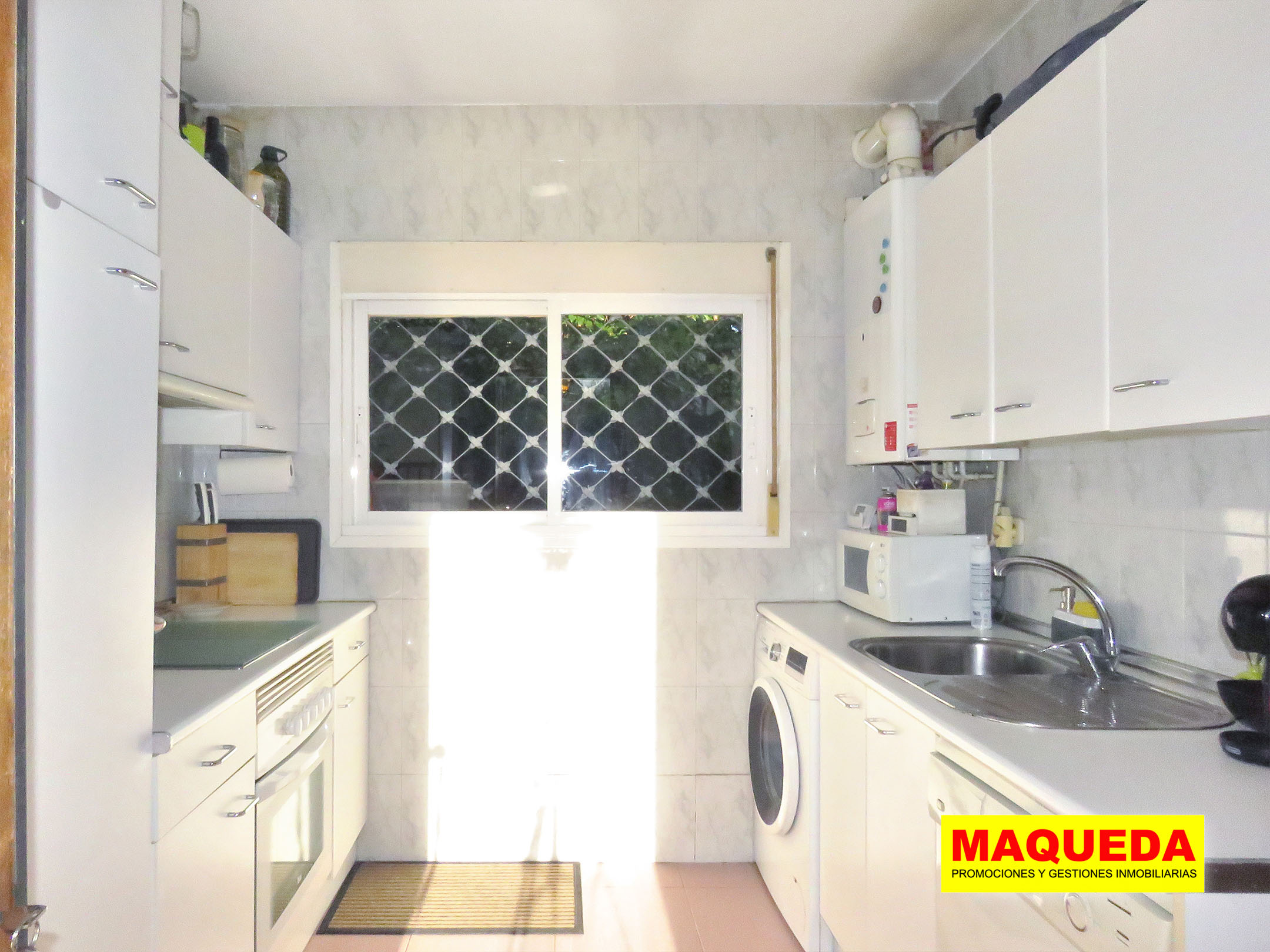 Cocina independiente con muebles blancos y ventana con rejas de seguridad