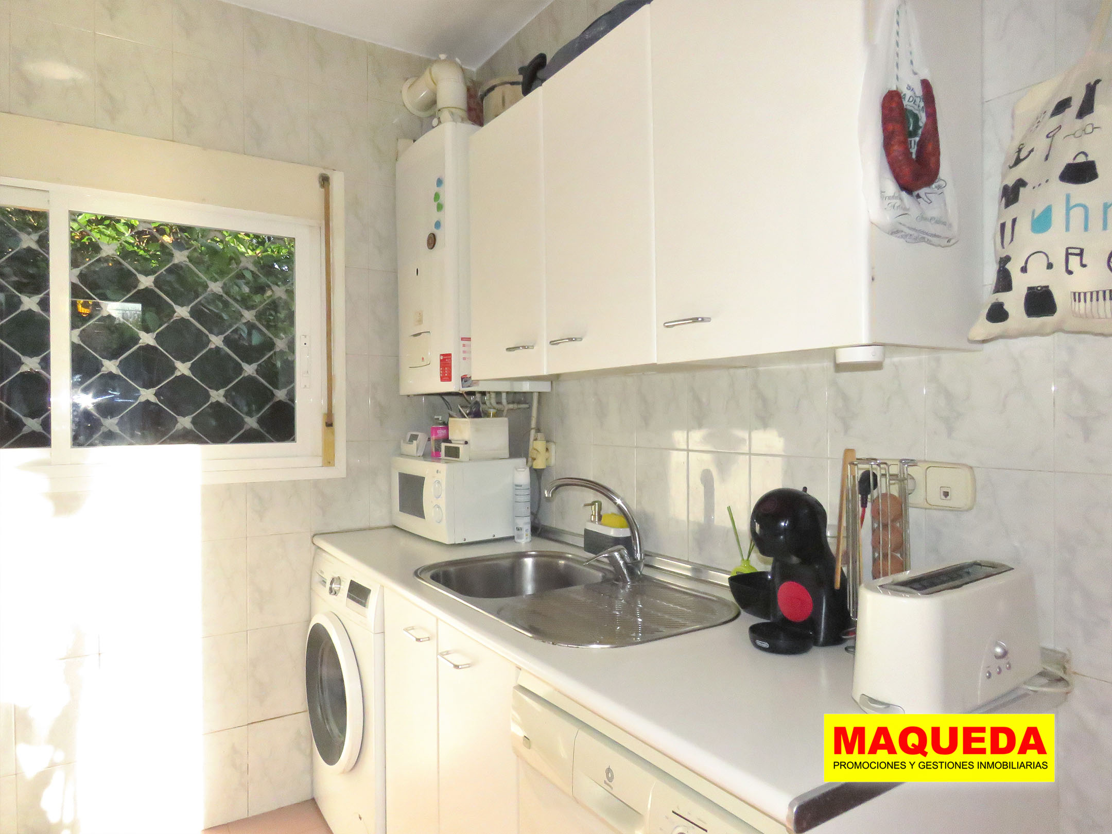 Cocina independiente con muebles blancos y ventana con rejas de seguridad