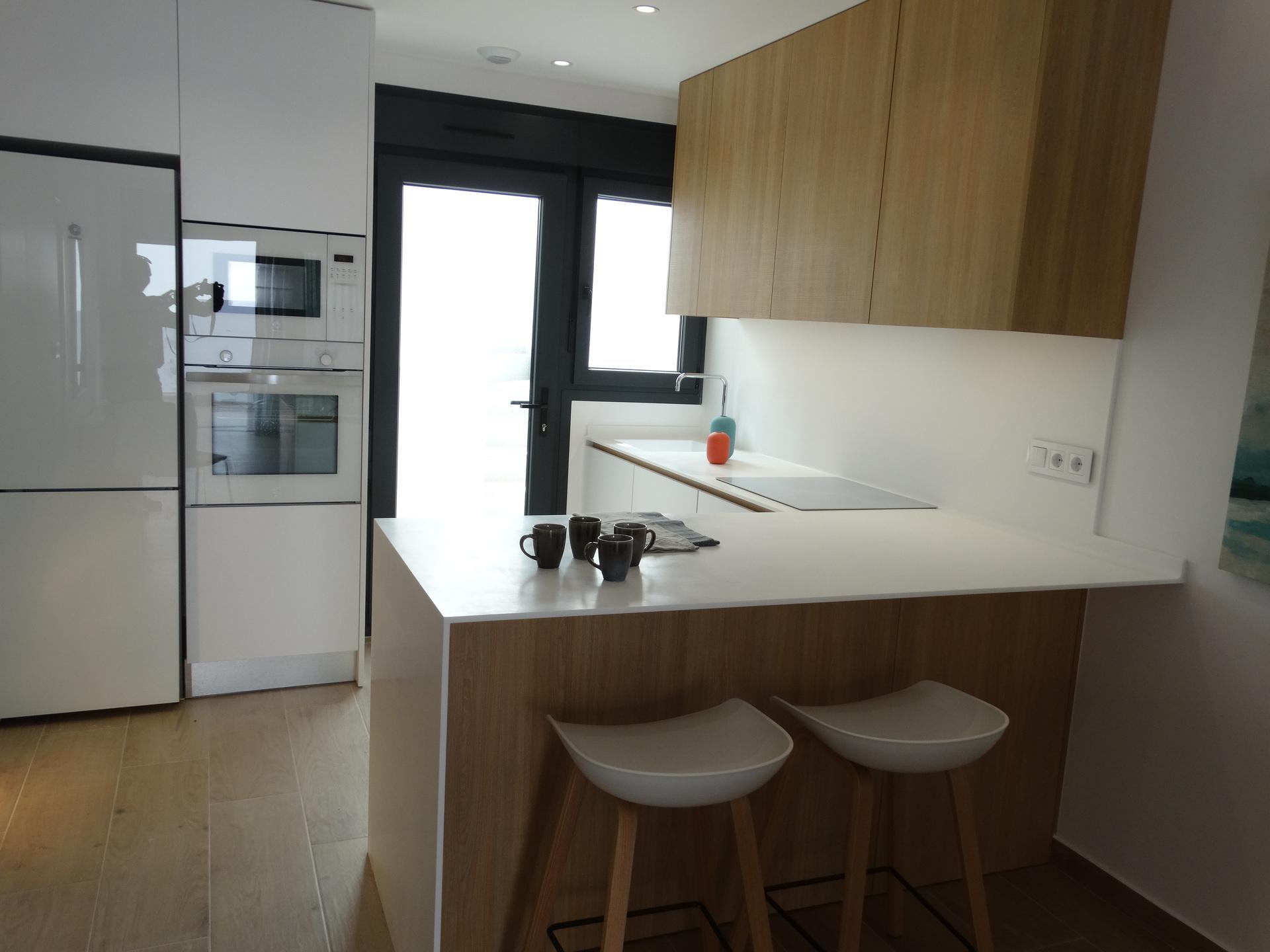 Modern kitchen with white island, wooden cabinets, and a built-in oven wall; tall white fridge on left.