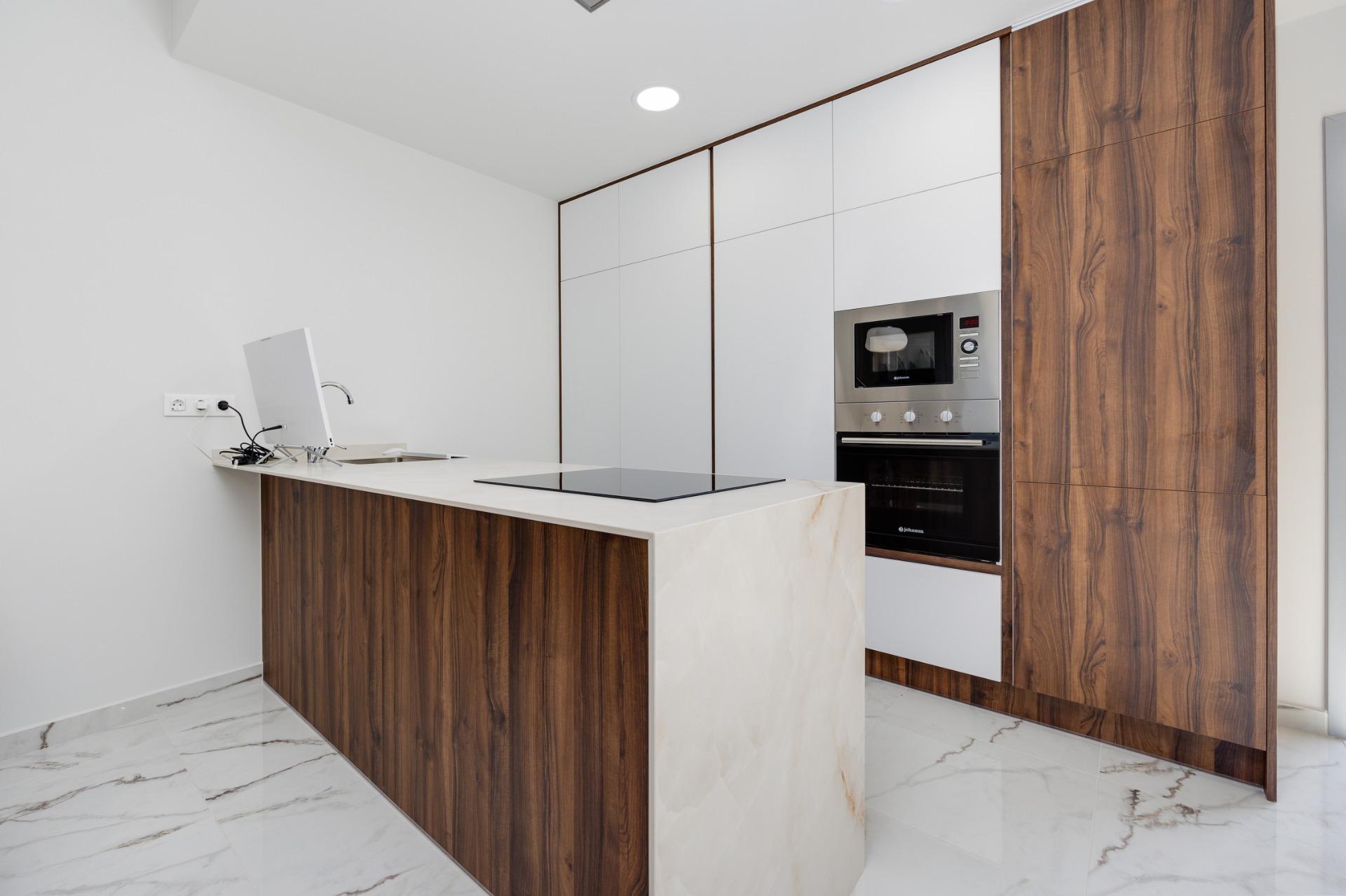 Modern kitchen with white upper cabinets, walnut wood panels, marble island, and stainless steel oven.