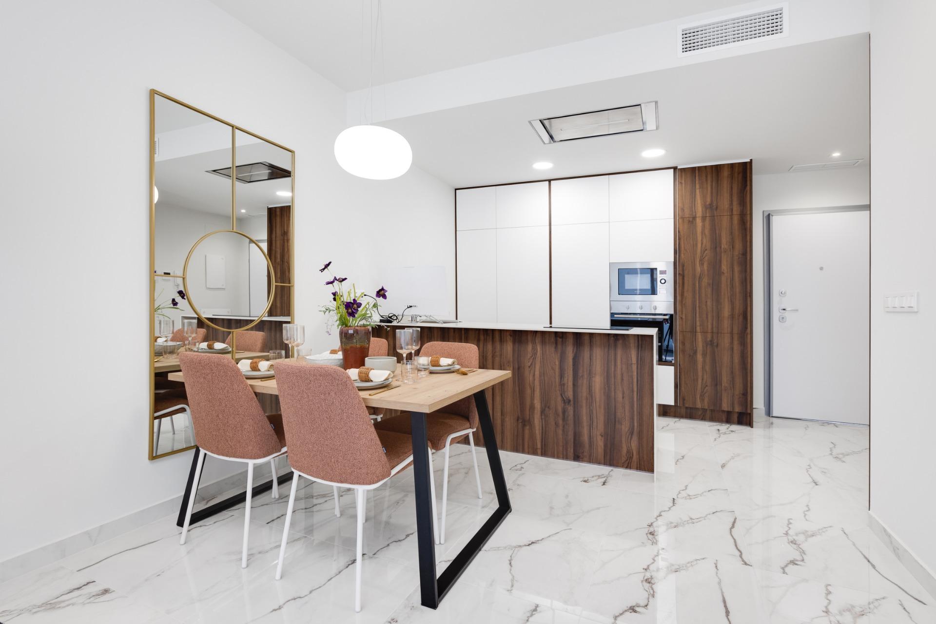 Dining area with a wooden table set for six, pink chairs, and a large gold-framed mirror against a white wall.