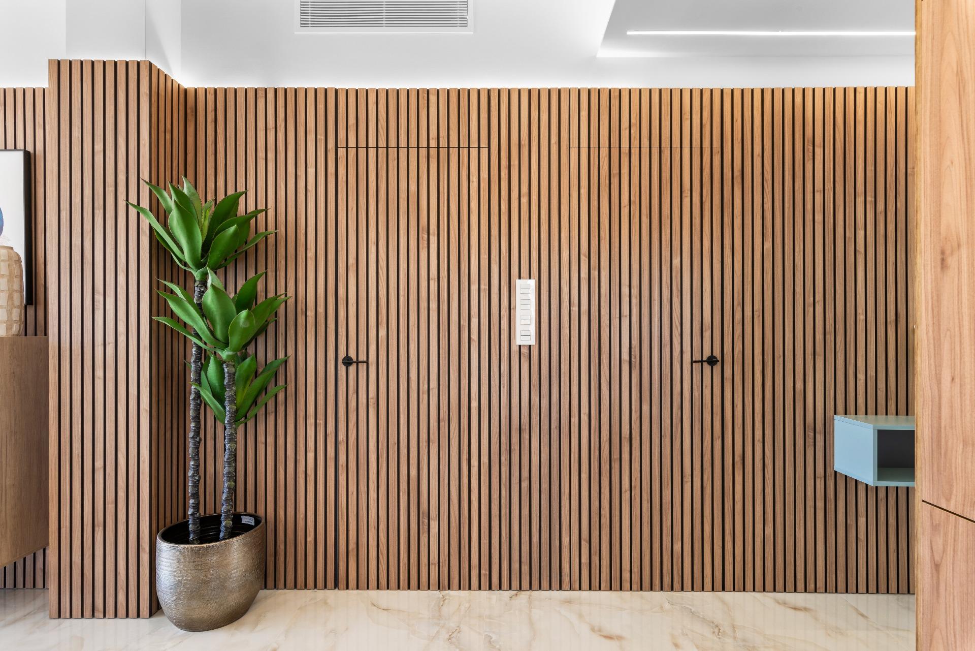 Wooden vertical slat wall with a tall potted plant on the left and marble floor below, modern interior.