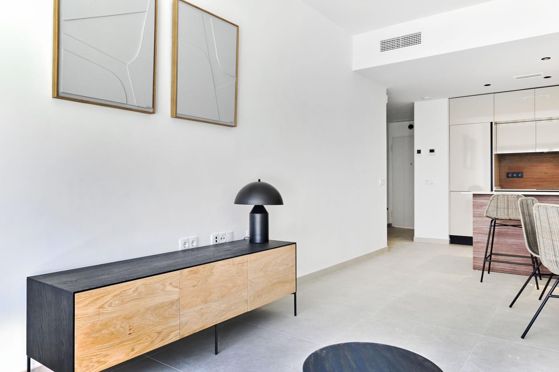 Open-plan living space with a long black-and-wood sideboard, black dome lamp, and two framed abstract artworks on a white wall coupé.