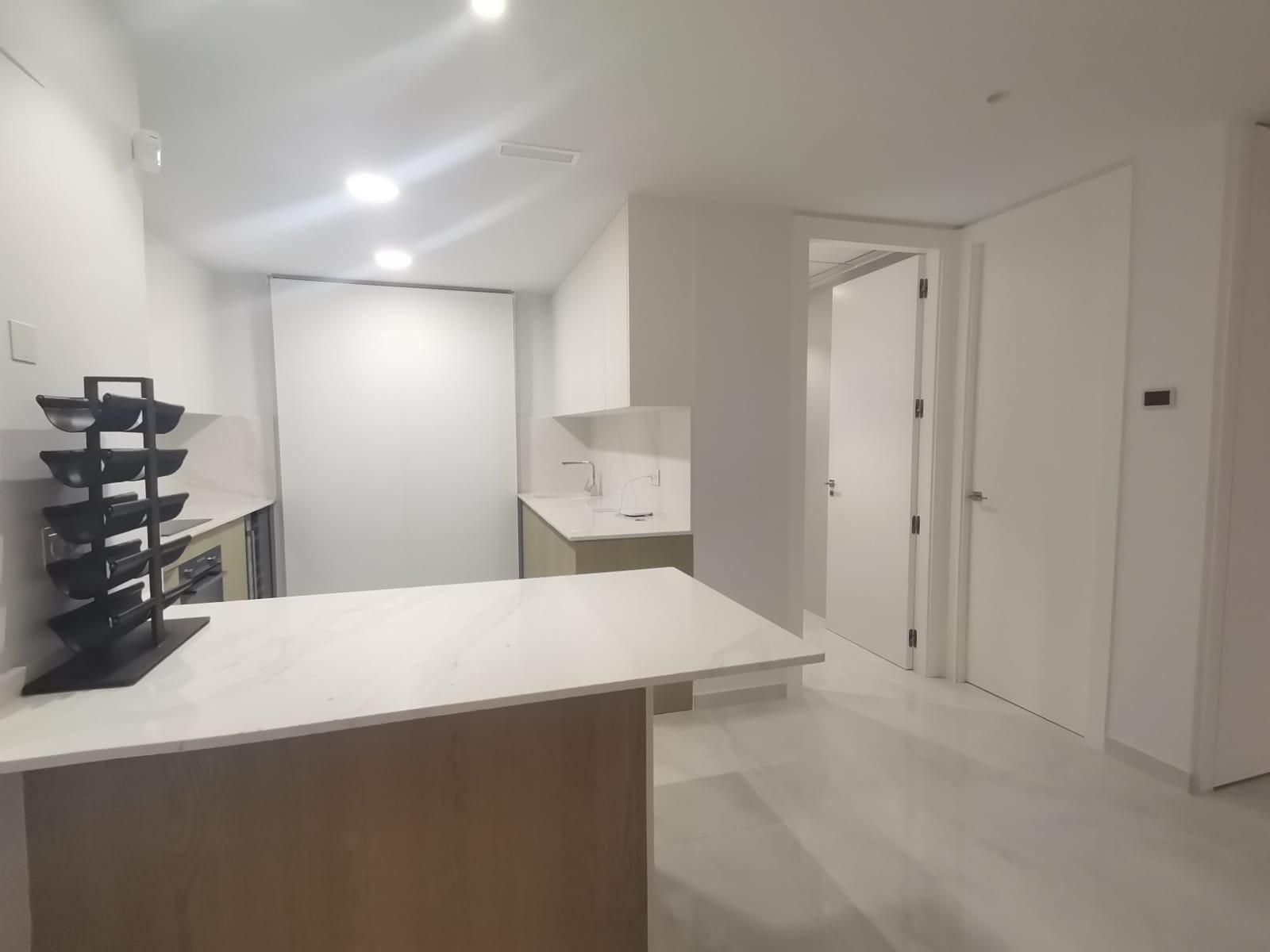 Bright minimalist kitchen with white cabinets, marble island, and a black multi-tier spice rack on the left.