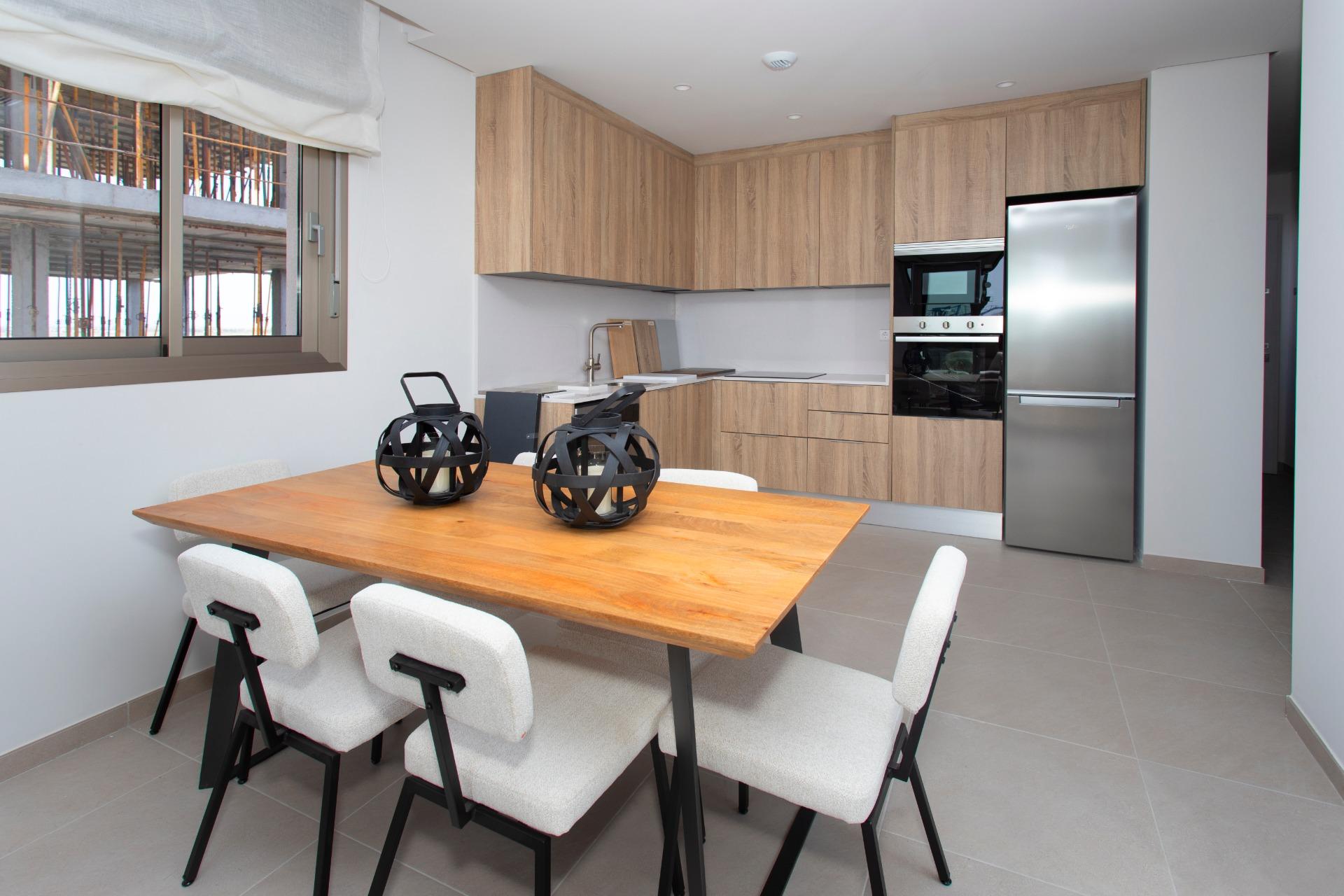 Modern kitchen with light wood cabinets, stainless-steel fridge, and built-in oven, plus a wooden dining table with white chairs.
