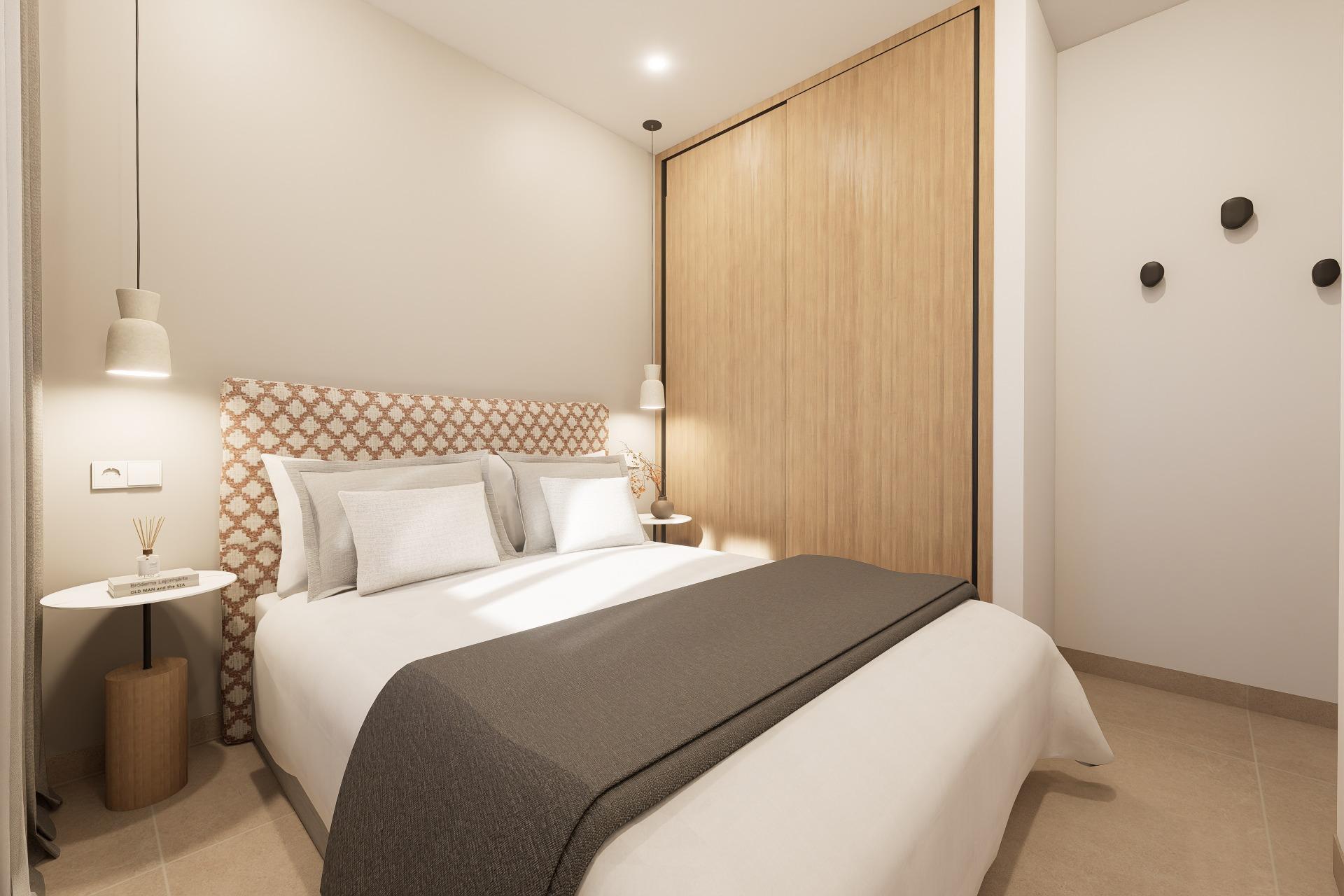 Double bed with a patterned headboard, two pendant lamps, round side tables, and a large wooden sliding wardrobe in a minimalist beige room.