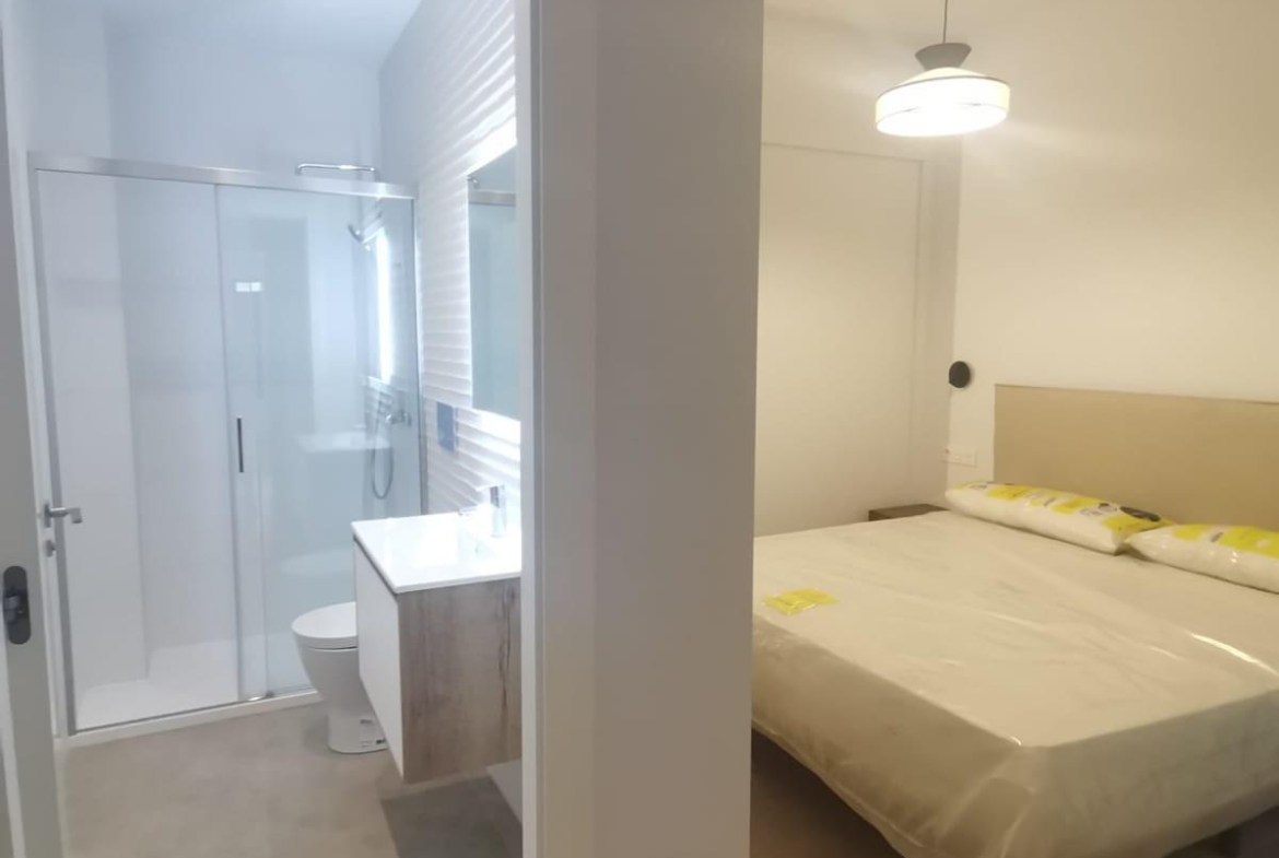 Hotel room with a partially open bathroom to the left and a double bed to the right, modern fixtures and neutral tones visible.