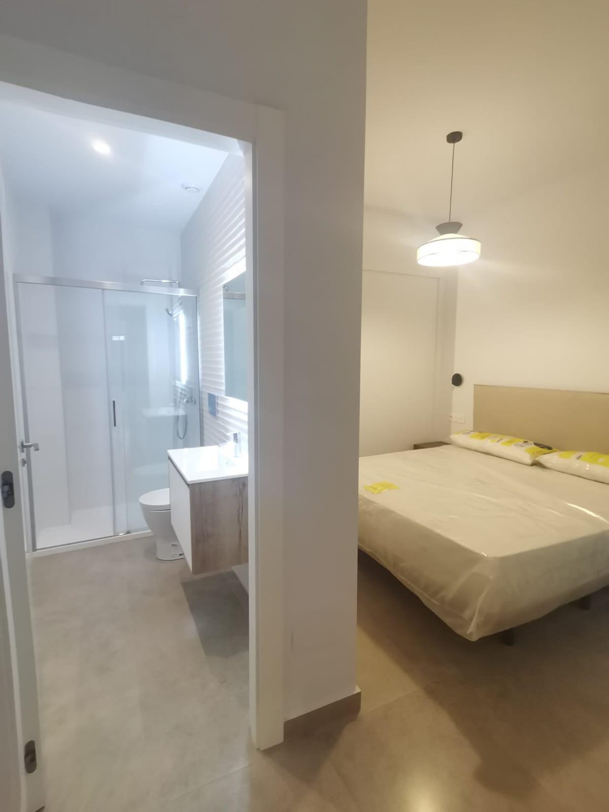 Hotel room with a partially open bathroom to the left and a double bed to the right, modern fixtures and neutral tones visible.