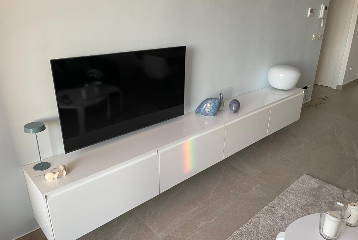 Flat-screen TV mounted above a glossy white media console with ceramic bird figurines and a white orb sculpture nearby.