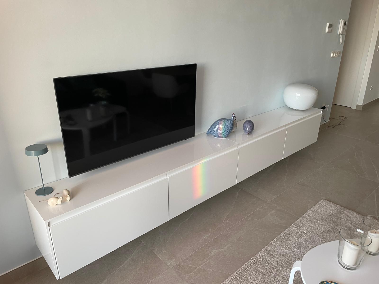 Flat-screen TV mounted above a glossy white media console with ceramic bird figurines and a white orb sculpture nearby.