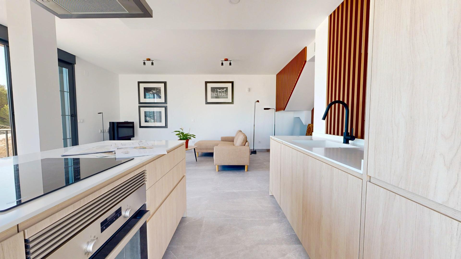 Open-concept kitchen and living area with light wood cabinets, white counters, and a beige seating arrangement visible beyond the island.