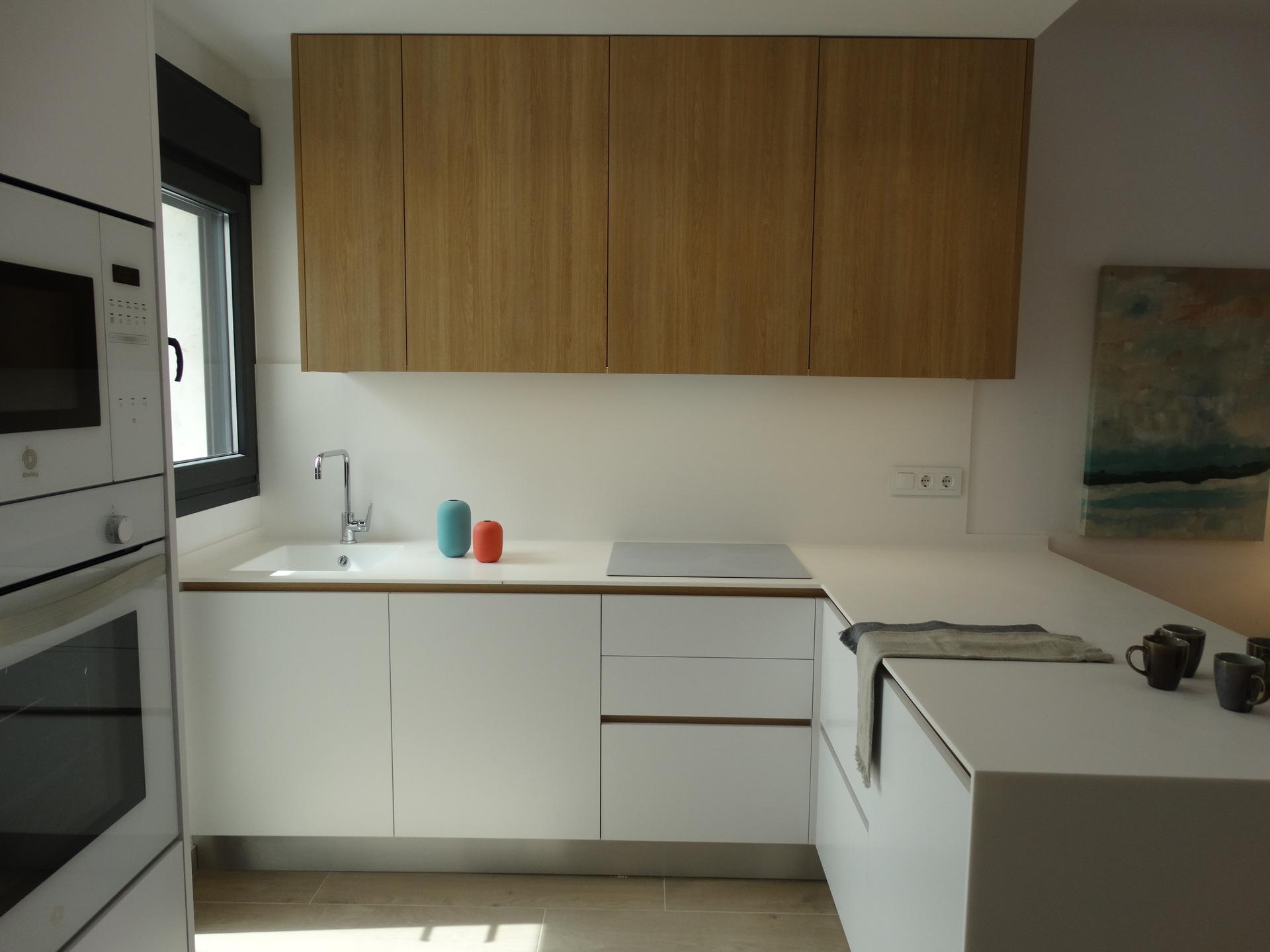 Minimalist kitchen with white base cabinets, wood upper cupboards, stainless steel sink, and a window on the left letting in light.