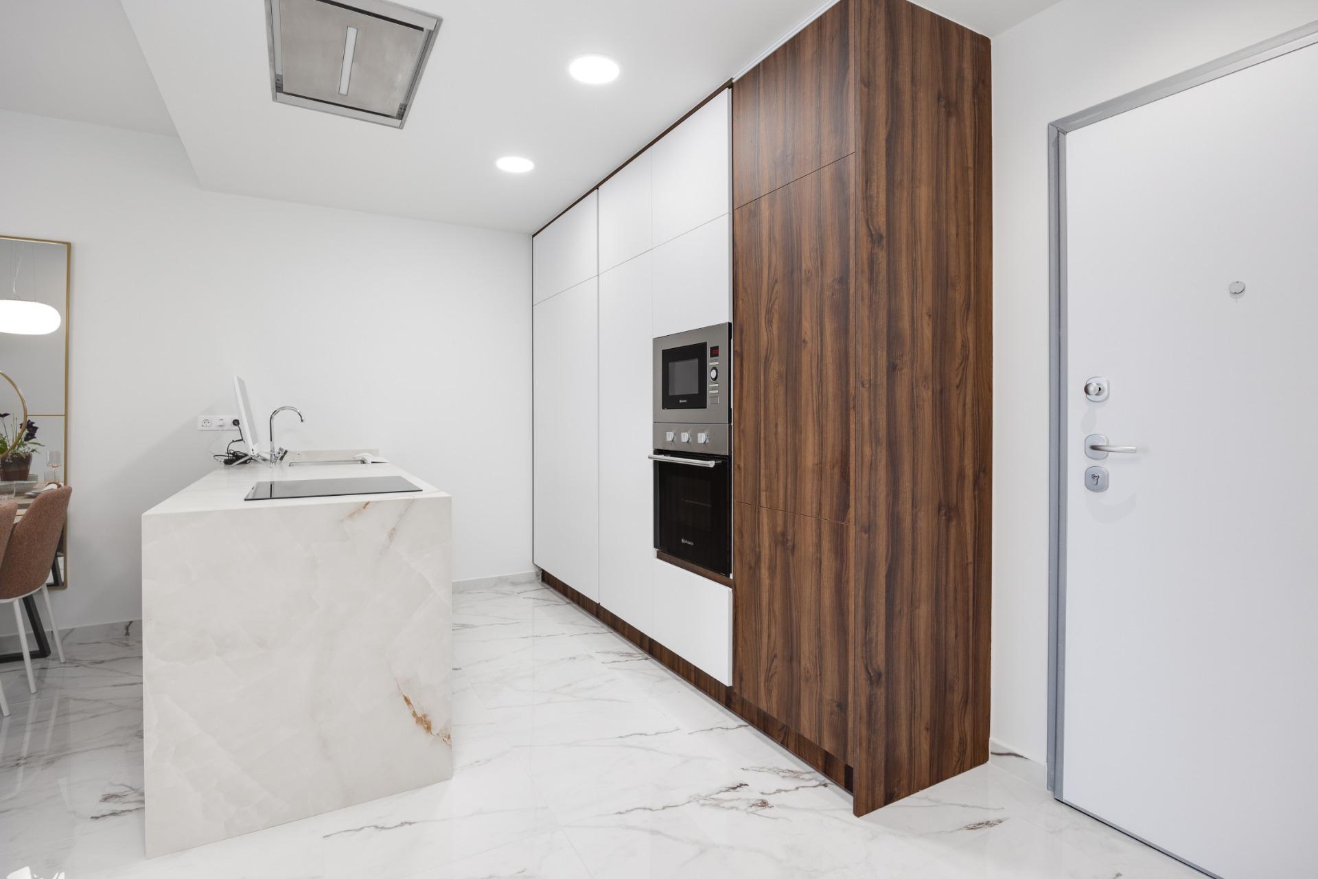 Modern kitchen with white cabinets, a marble island, and a tall wood-paneled wall housing a built‑in oven and microwave.