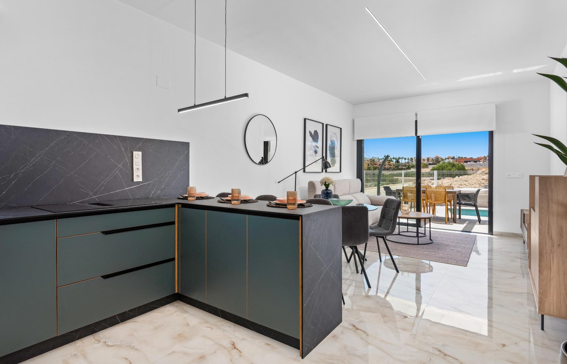 Open-plan kitchen and living area with dark teal cabinetry, marble countertops, and a dining table; sliding doors open to a sunny outdoor patio.