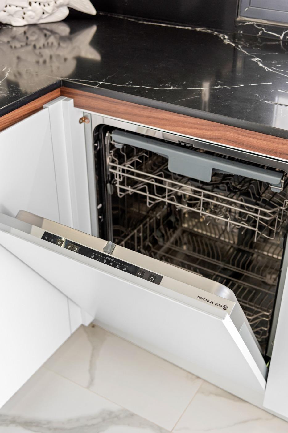 Open built-in dishwasher under a marble countertop, showing empty racks and control panel visible on the door.