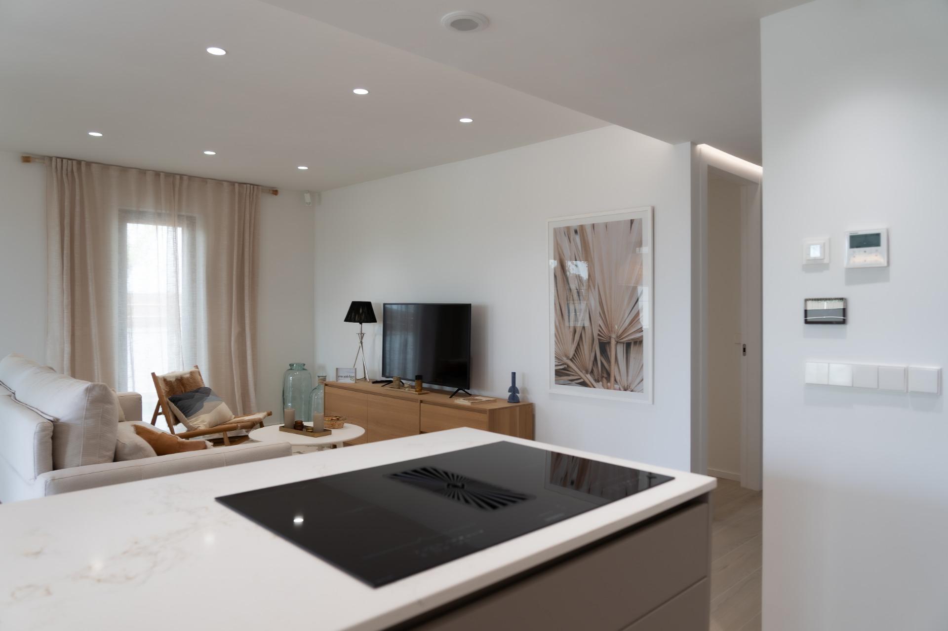 Open-plan living room with a white sofa, wooden TV console, and a large framed abstract print on the wall to the right.
