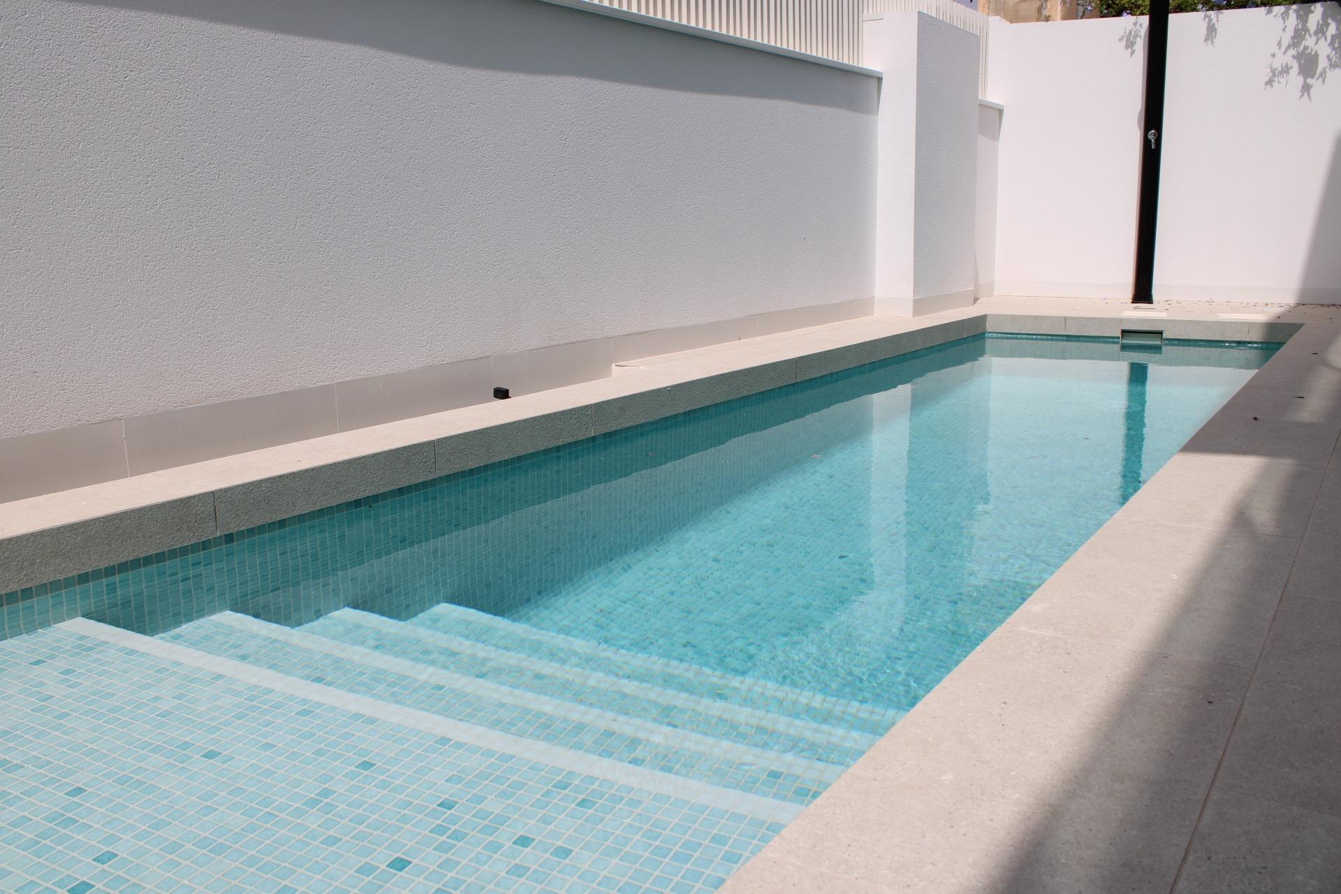 Modern rectangular pool with turquoise tiled interior, white surrounding walls, and a concrete deck.