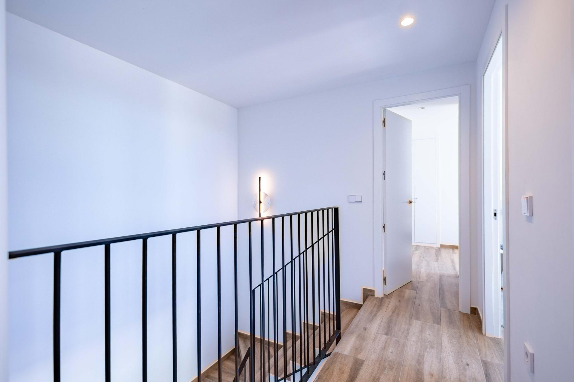 Bright upstairs hallway with a black metal railing, light wood floor, and an open door to a bright room outside the frame.