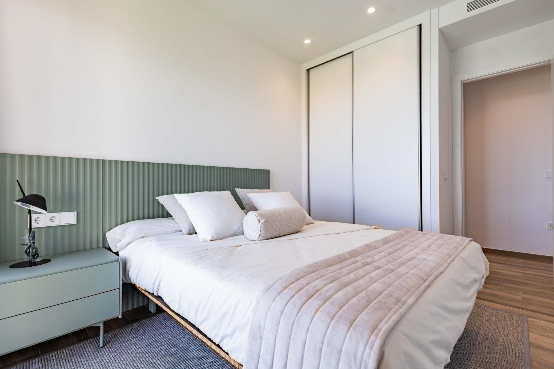 Bedroom with a queen bed, white linens, and a green ribbed headboard against white walls; sliding closet doors on the right.