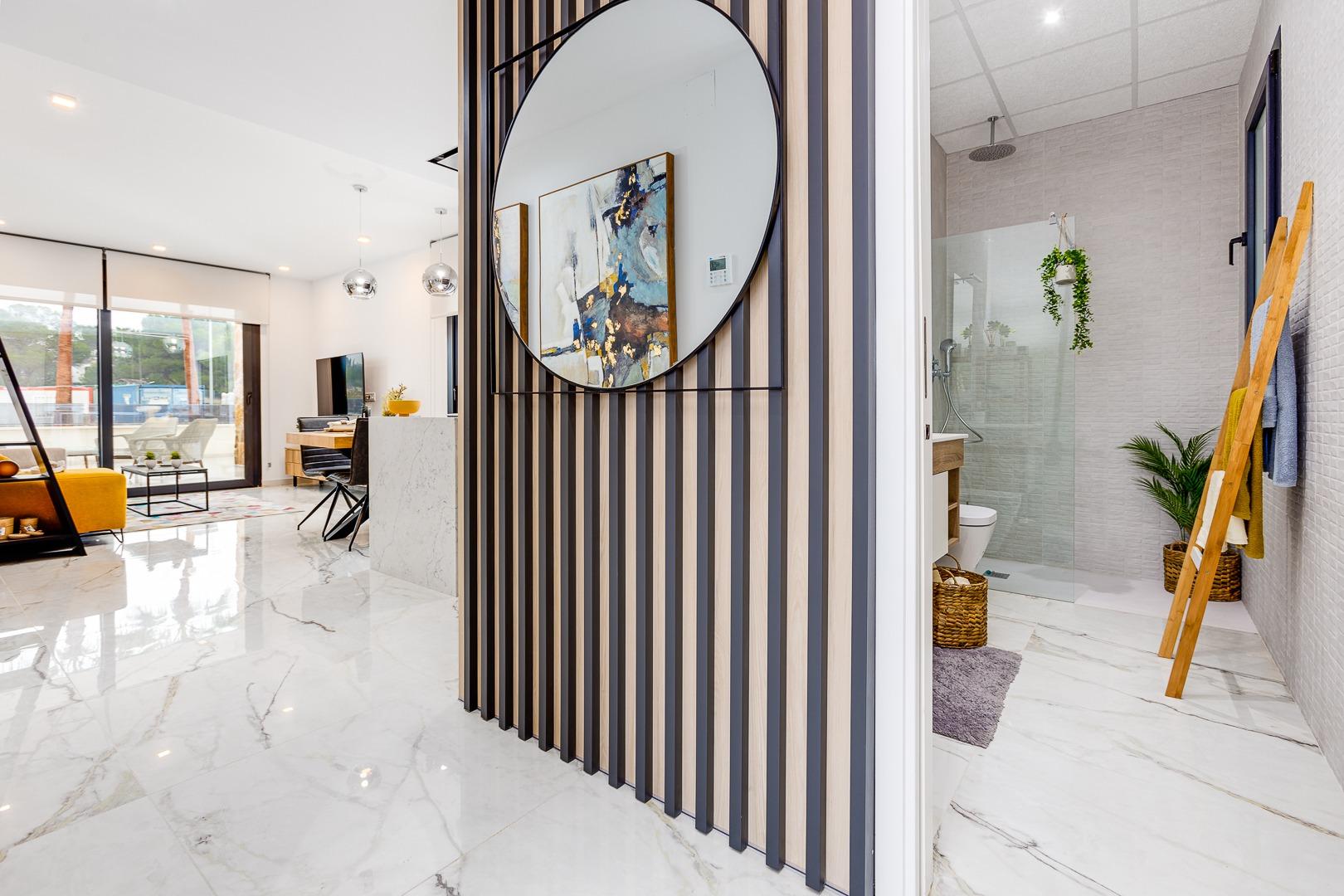 Open, modern living area with marble floors, a circular mirror on a wood-slatted divider, and glass doors to a sunlit balcony.
