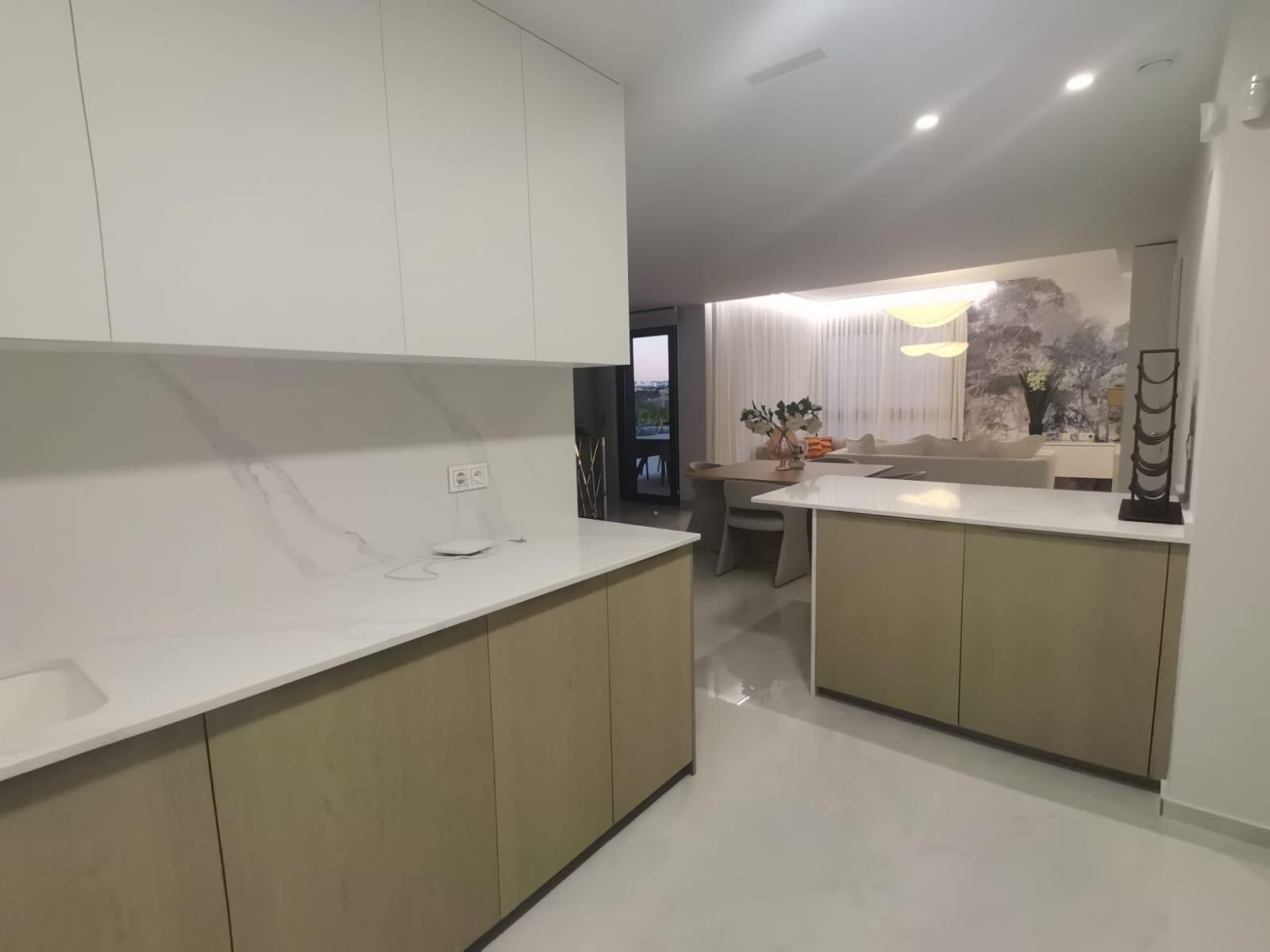 Modern L-shaped kitchen with white upper cabinets, light wood lower cabinets, and white marble countertops and backsplash.