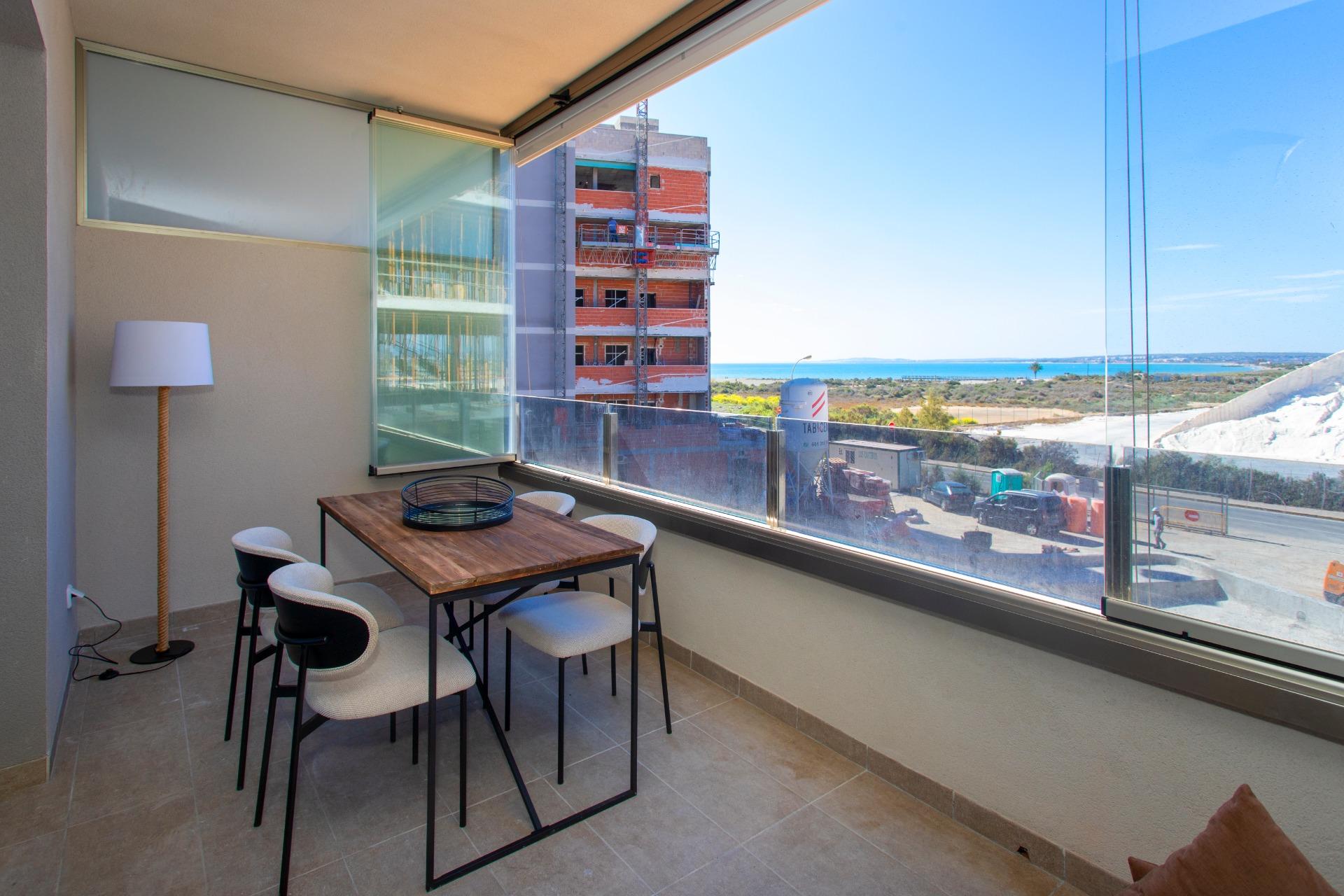 Indoor balcony dining area with a wooden table and six upholstered chairs, glass railing and an ocean view outside.