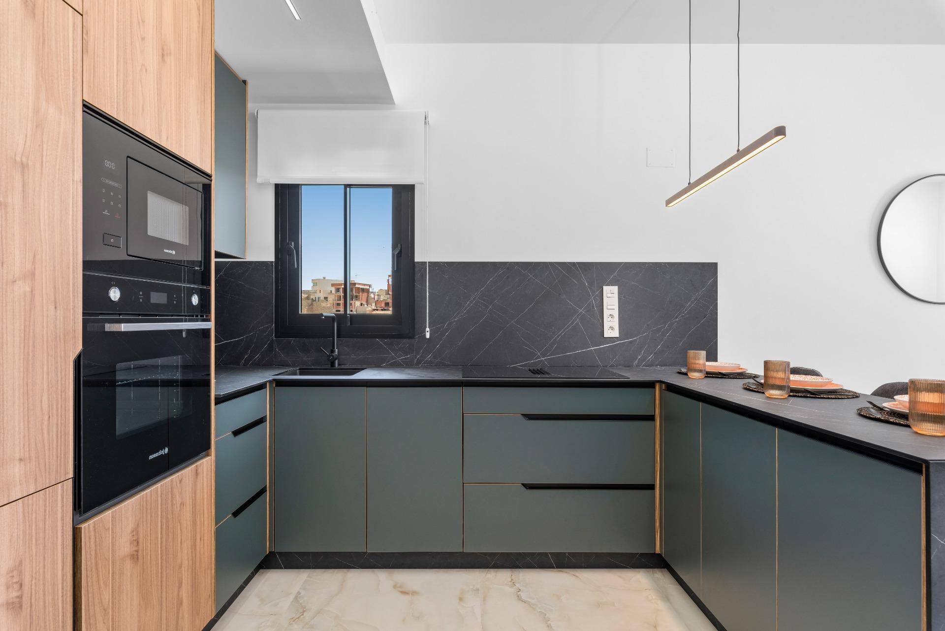 Modern kitchen with dark green cabinets, gold trim, black marble backsplash, and a built‑in oven beside a tall wooden cabinet.