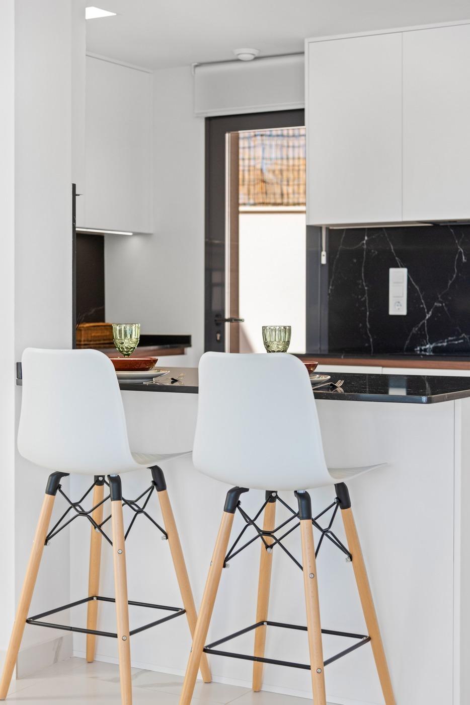 Modern white kitchen with a black marble island, two white bar stools, and place settings (glasses, plates) ready for dining