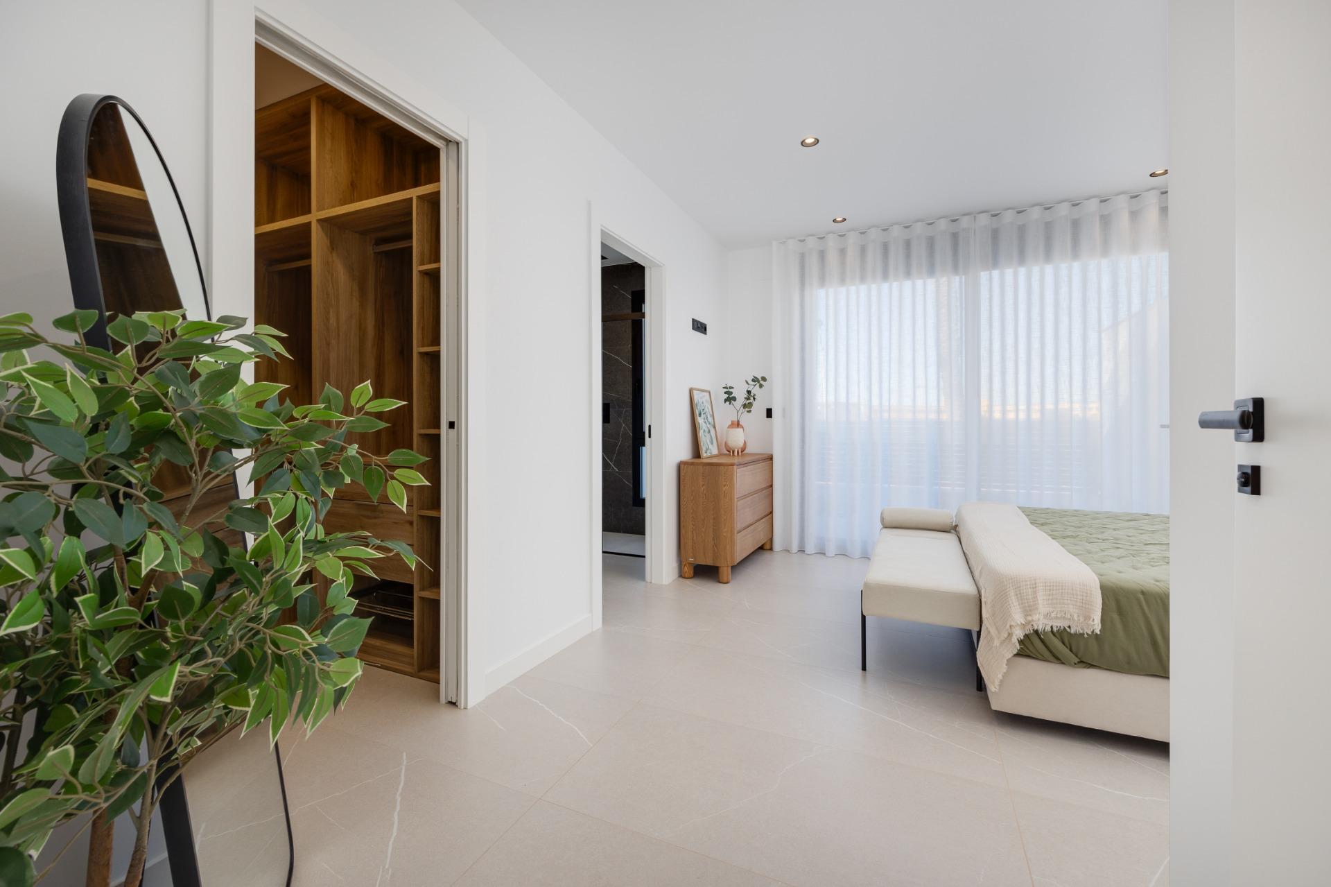 Bright, minimalist bedroom with a bed, sheer white curtains, and an open walk-in closet with wooden shelving visible in the doorway.