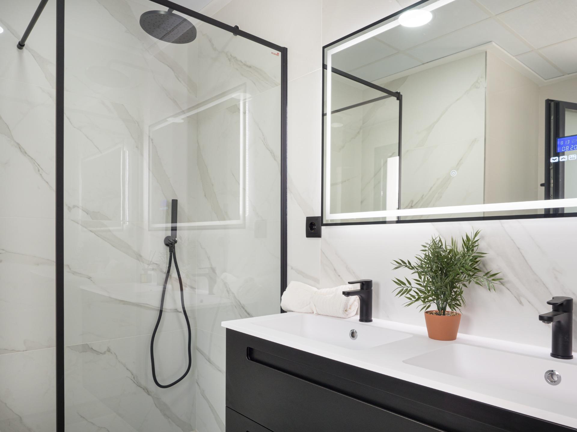 Modern bathroom featuring a double-sink vanity, black fixtures, and a backlit rectangular mirror with marble-tile walls.