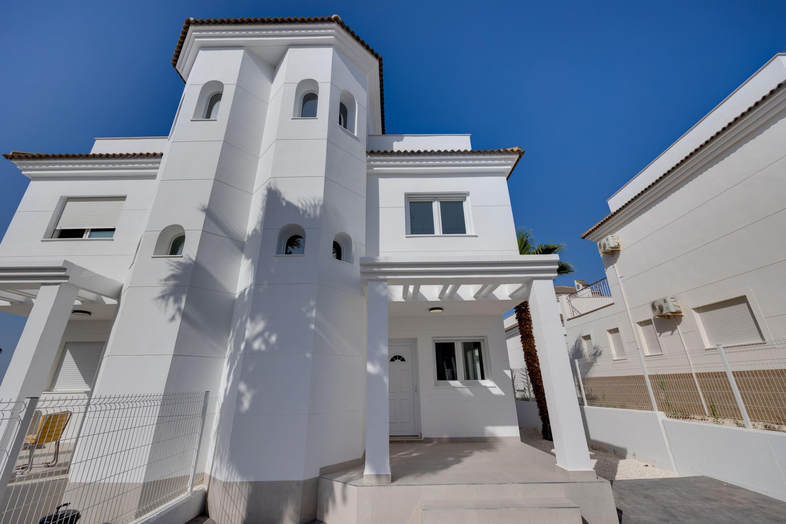 White modern villa exterior with arched windows, white walls, and terracotta roof tiles under a bright blue sky