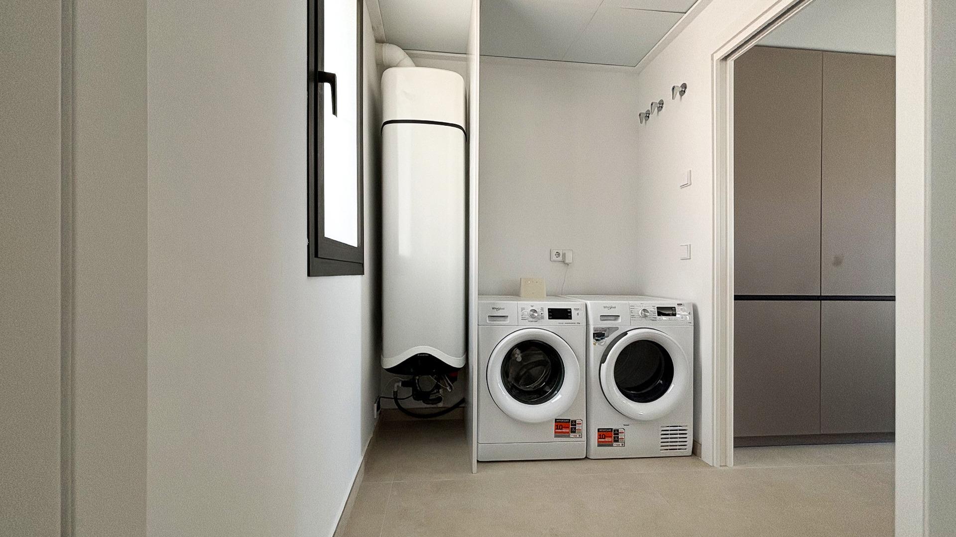 Laundry room with a front-loading washer and dryer side by side, a tall white water heater, and wall hooks above; neutral tones and a closed cabinet on the right