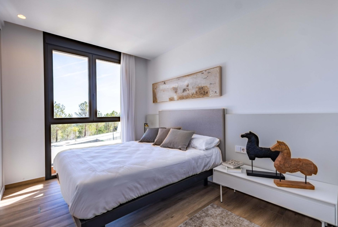 Modern bedroom with a large black-framed window, white bedding, and a light gray headboard; abstract wall art above the bed.