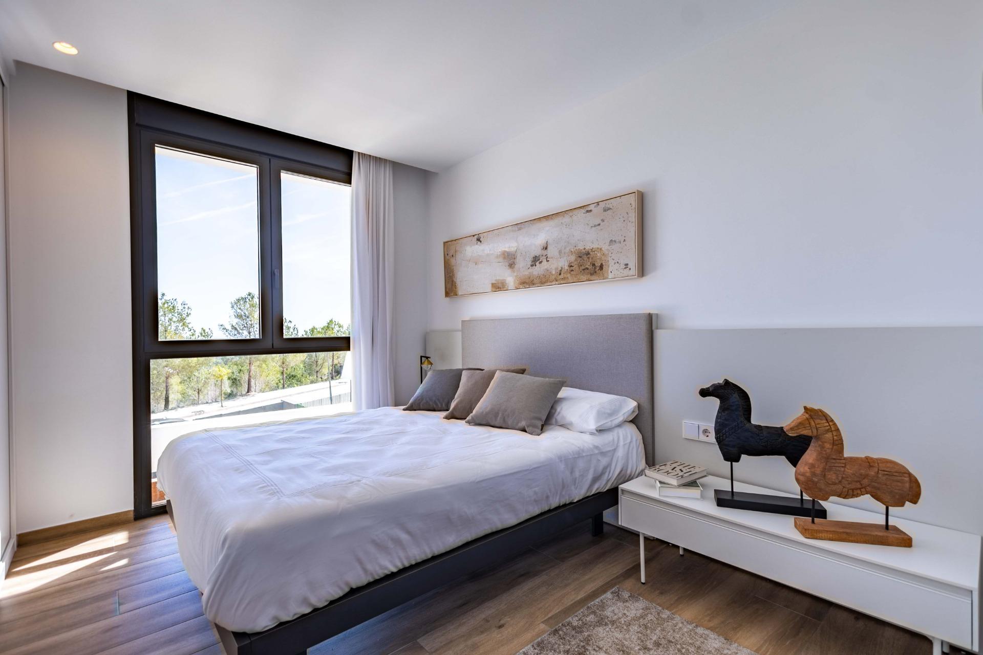 Modern bedroom with a large black-framed window, white bedding, and a light gray headboard; abstract wall art above the bed.
