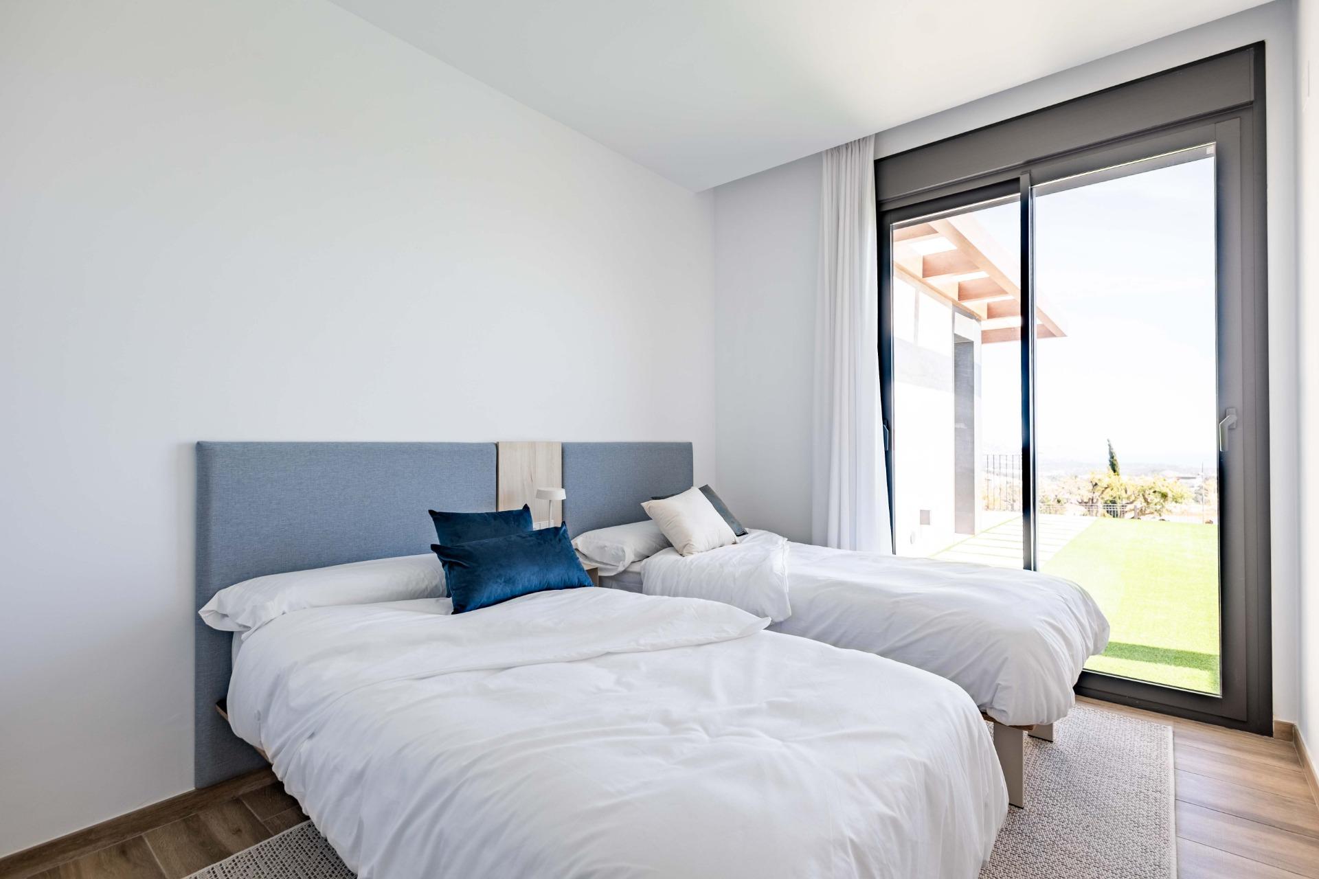 Twin bedroom with white bedding, blue pillows, and a large sliding glass door opening to a sunny outdoor area.