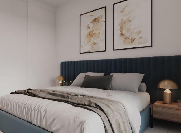 Contemporary bedroom with a tufted blue headboard, white bedding, gray throw, and two framed botanical prints above the bed, plus gold bedside lamps on wooden tables.
