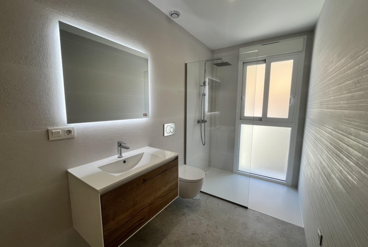 Modern bathroom with a white and wood vanity, backlit mirror, and glass shower enclosure.