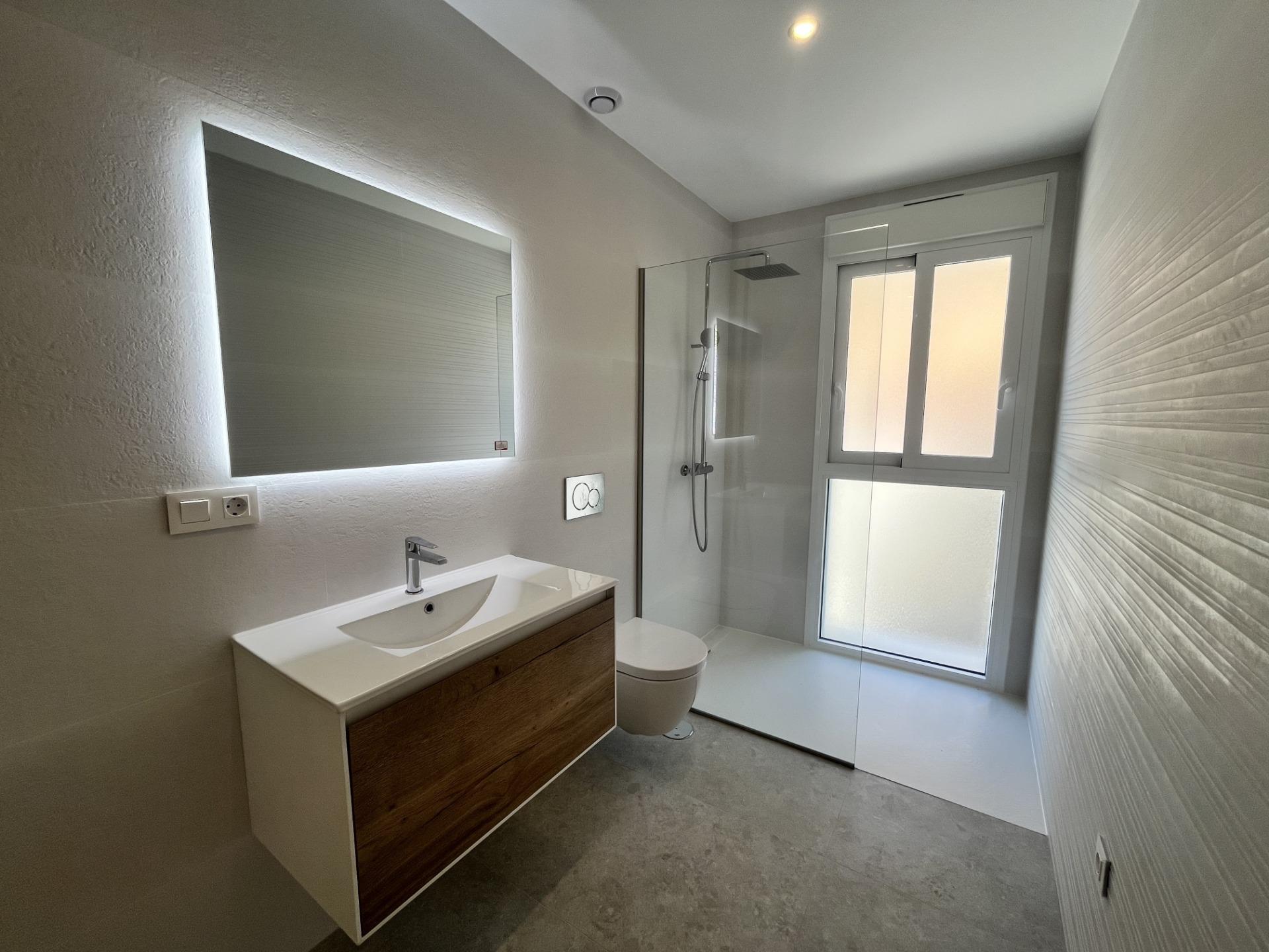 Modern bathroom with a white and wood vanity, backlit mirror, and glass shower enclosure.