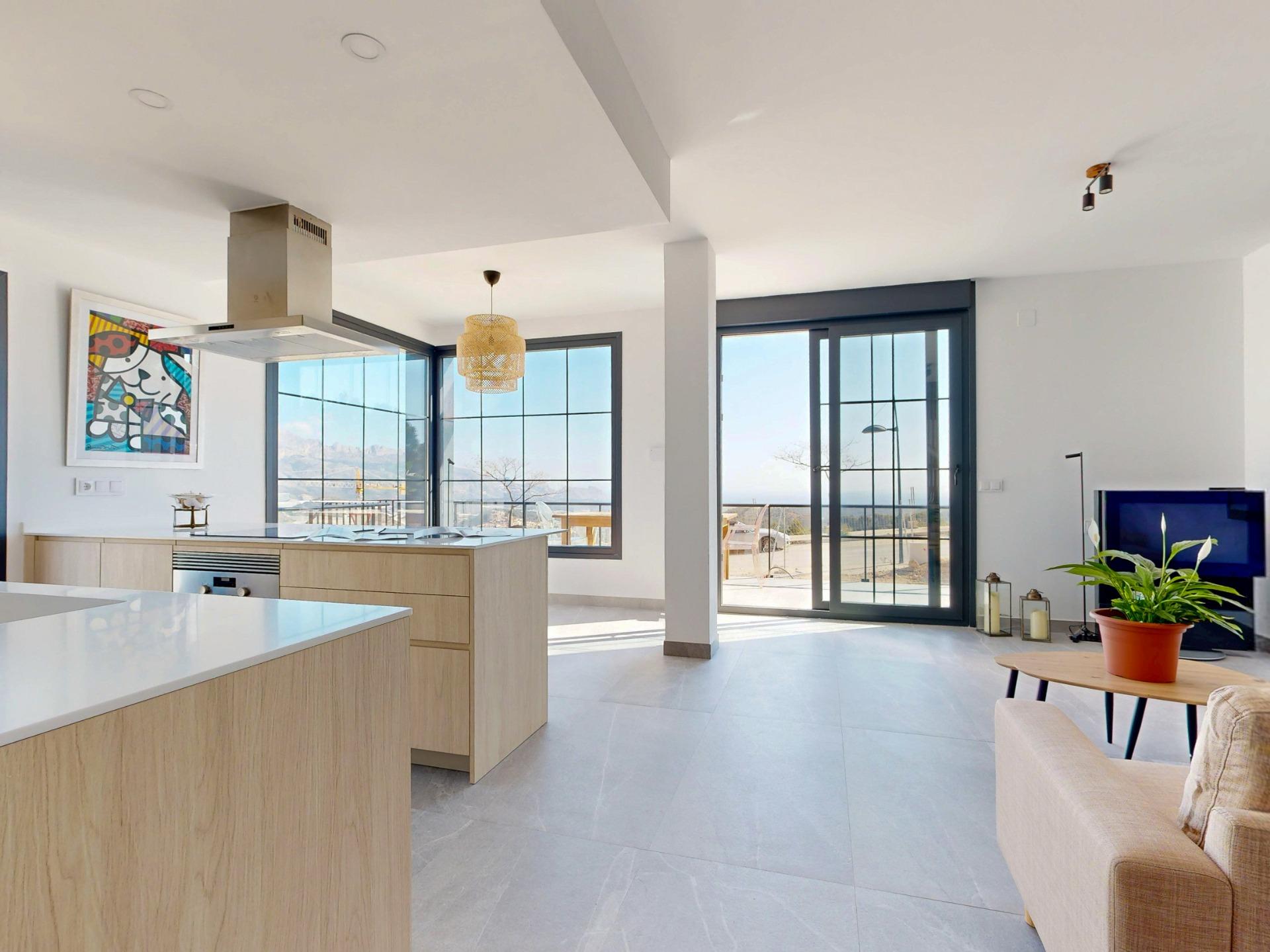 Open-plan kitchen with island, stainless range hood, and large windows overlooking a balcony outside the home.