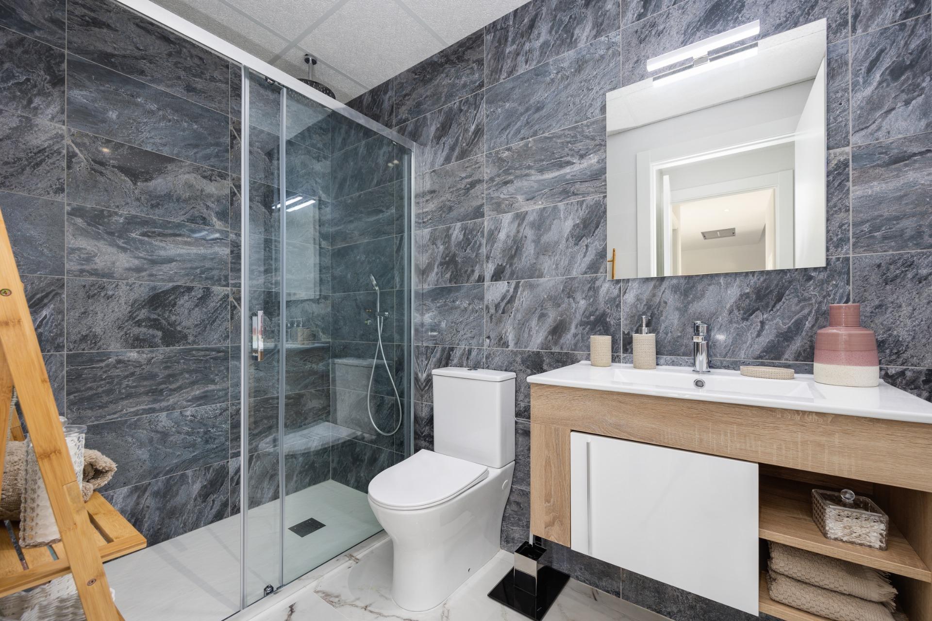 Modern bathroom with dark marble walls, glass shower enclosure, white toilet, and wood-finish vanity.