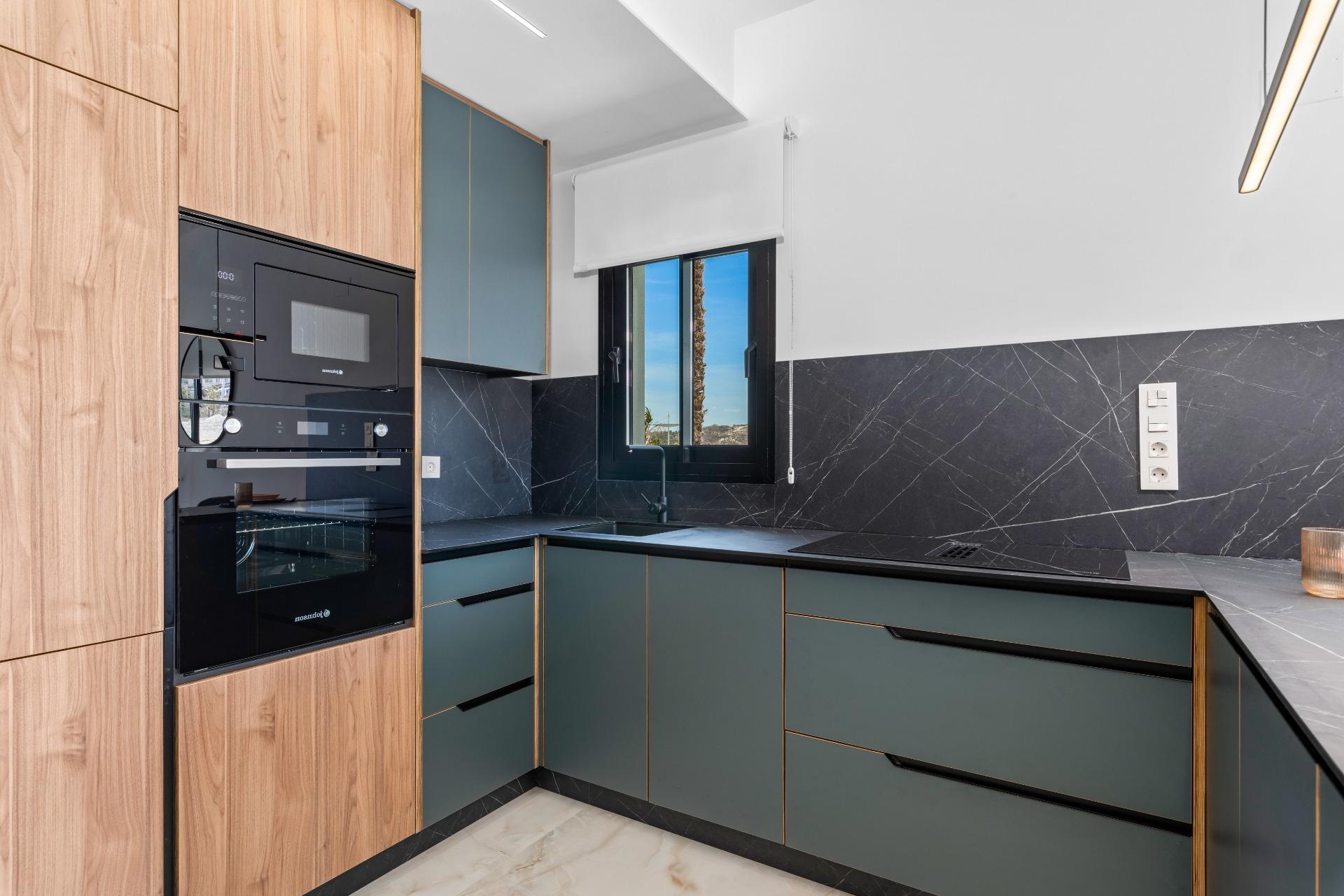 Modern kitchen with black built-in oven/microwave and tall wood cabinets beside teal lower cabinetry