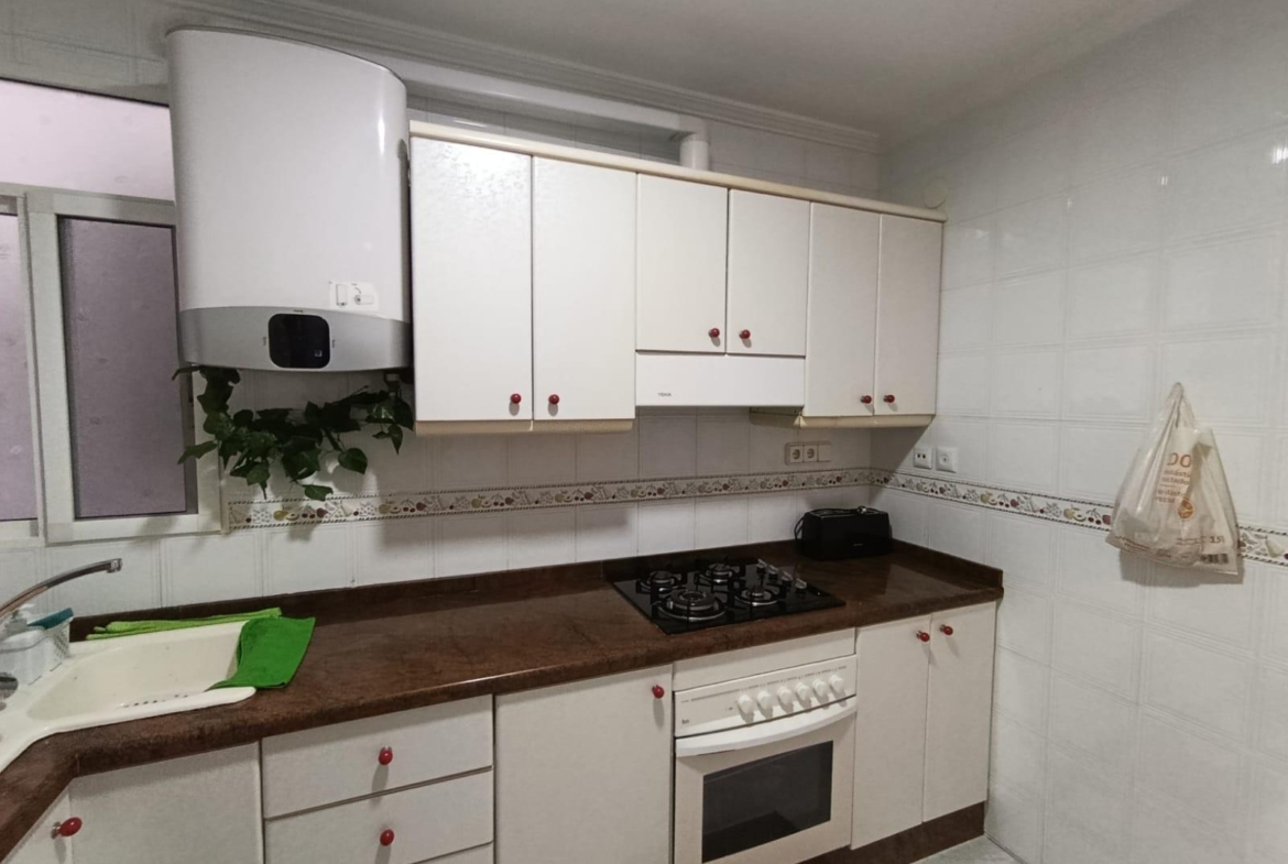 White kitchen with a brown countertop, wall-mounted cabinets, and a gas stovetop next to an oven. A boiler and a plant sit above the counter.