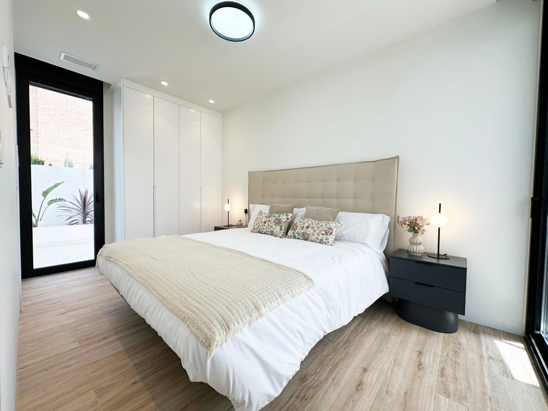 Modern bedroom with a large bed, beige upholstered headboard, white bedding, and two dark bedside tables with lamps.